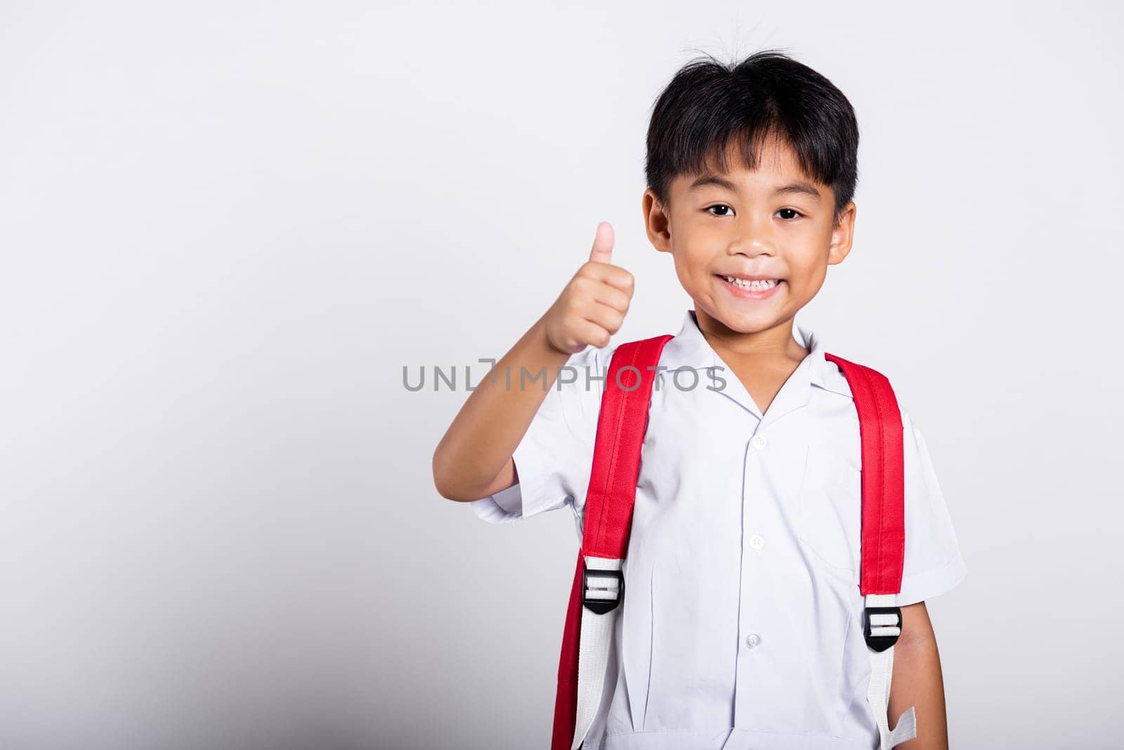 Asian adorable toddler smiling happy wearing student thai uniform red pants show thumb up finger in studio shot isolated on white background, Portrait little children boy preschool, Kid Back to school