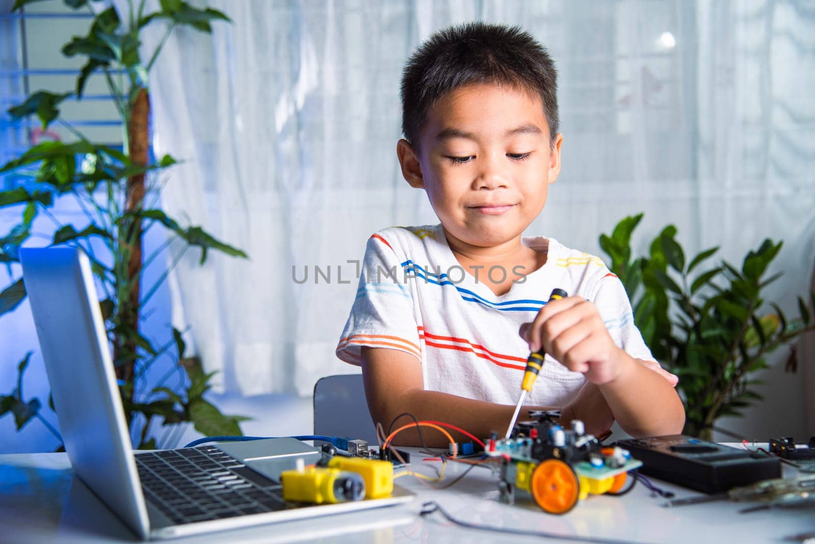 Asian kid boy assembling the Arduino robot car homework project at home, Little child tighten the nut with a screwdriver to assemble car toy, creating electronic AI technology workshop school lesson