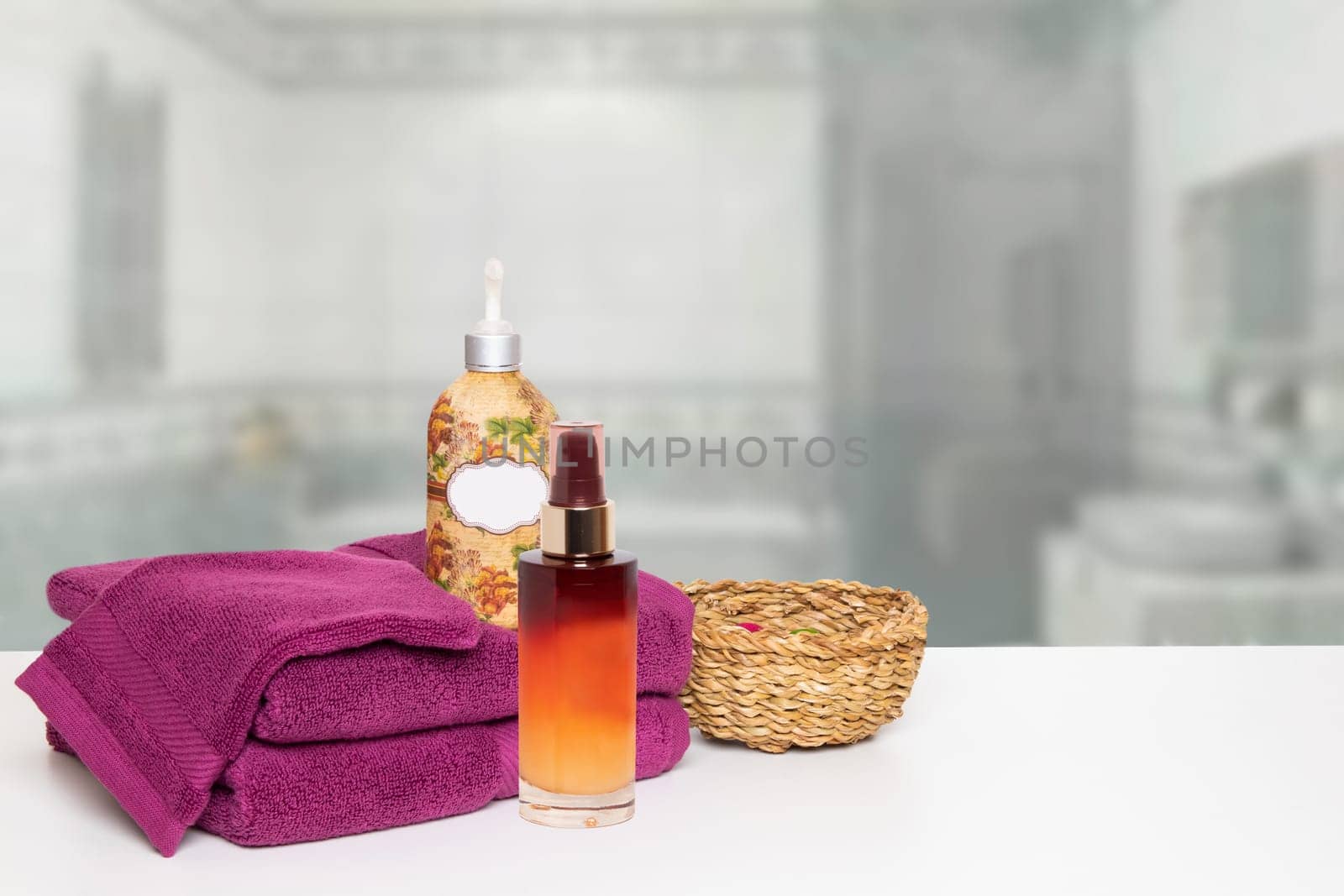 A beautiful composition of spa treatment on the table with towels, massage oil, cream and a basket over blurred bathroom. Space for product display montage.