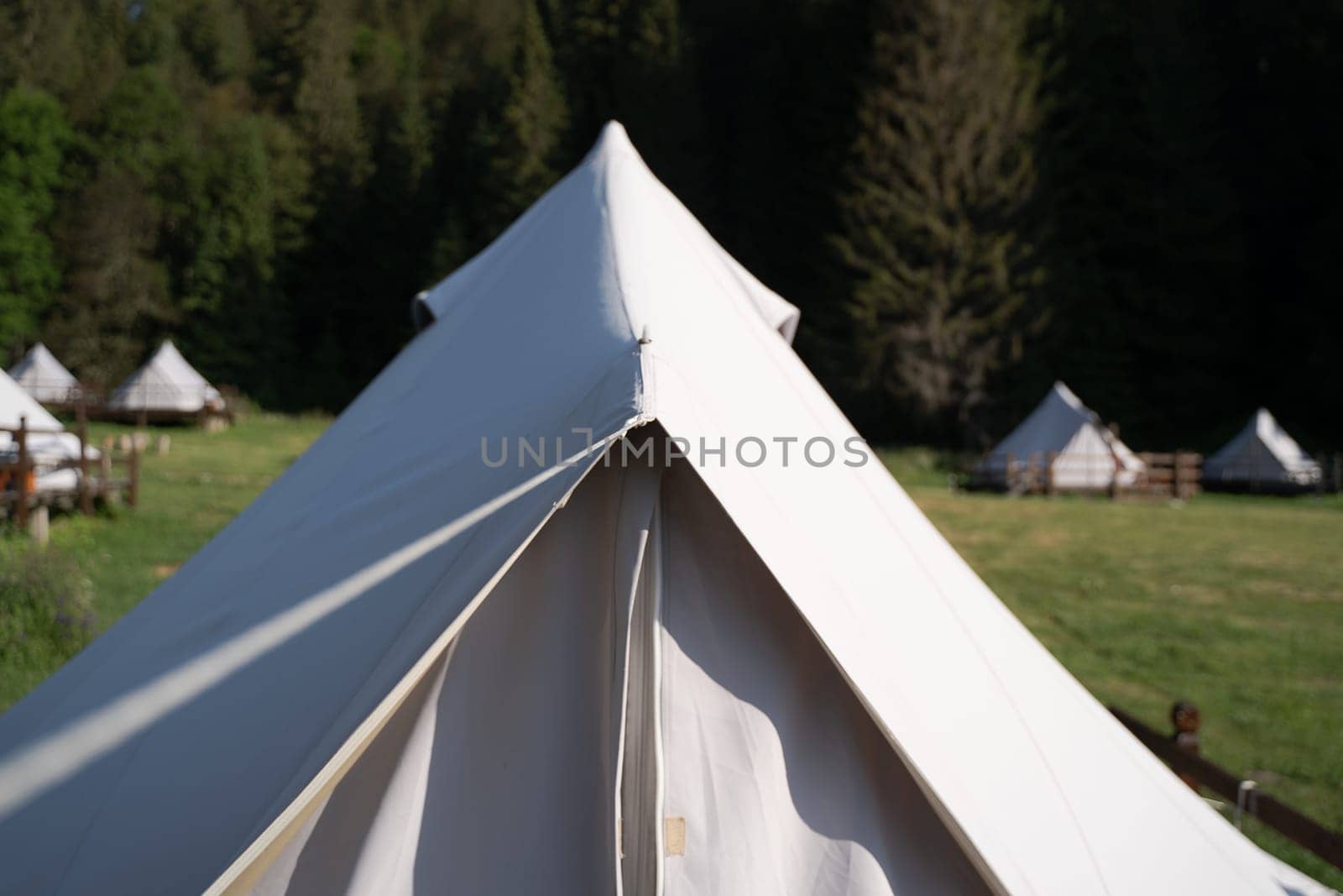 front view closeup of glamping tent top white fabric in green meadow surrounded by fir tree forest