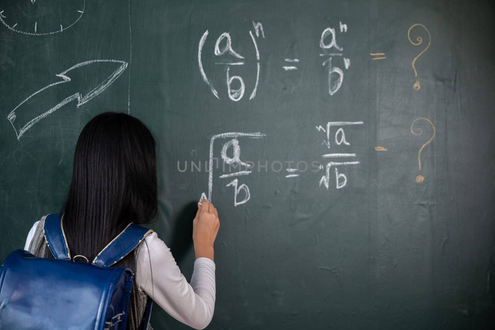 Education. Back view of school girl on science lesson in classroom write an answer on blackboard, primary child is standing in front of class in school writing chalkboard, Back to school concept