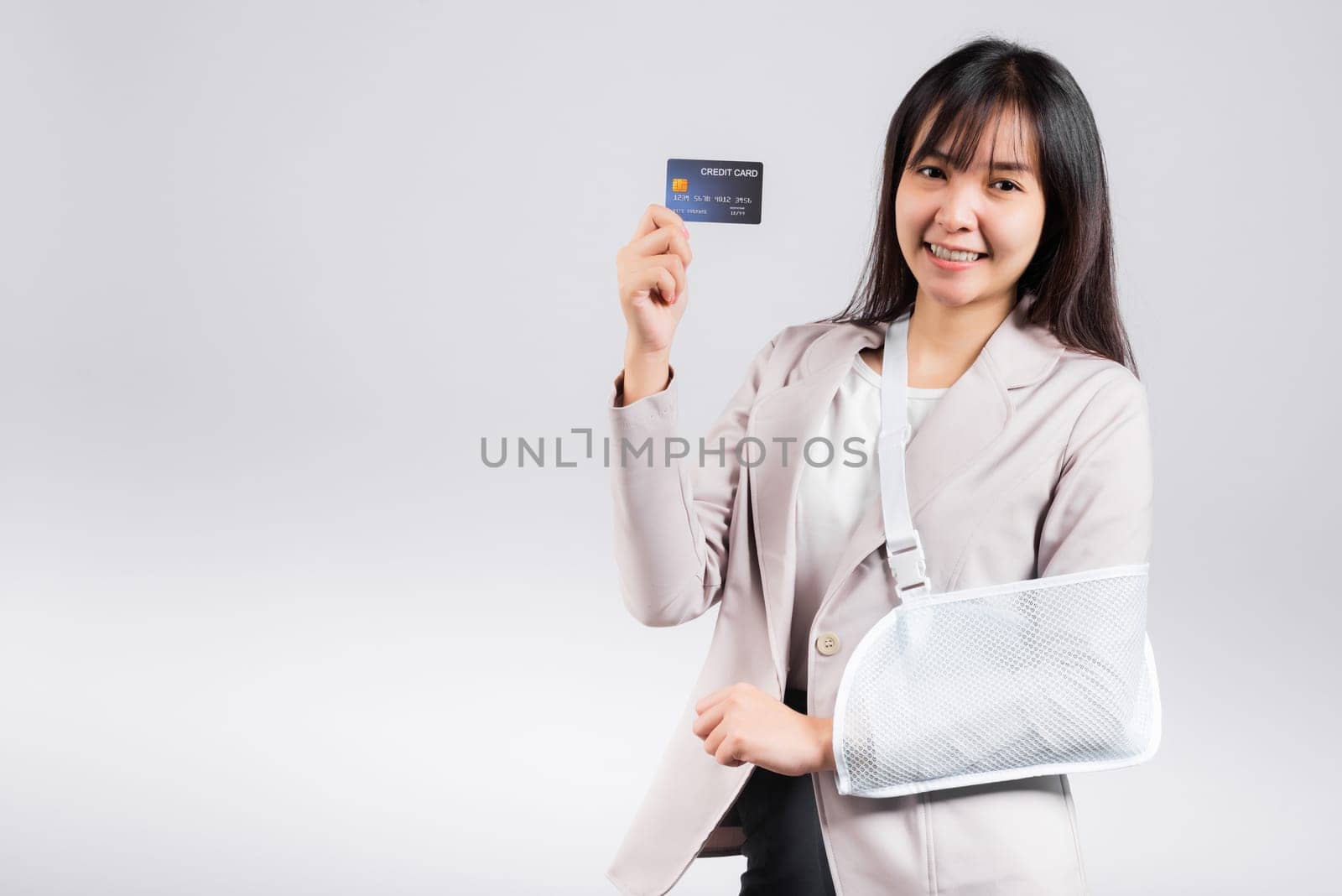 Woman confident smile broken arm after accident and wear arm splint for treatment she emergency pay medical bills by credit card, Happy Asian female sling support hand isolated on white background