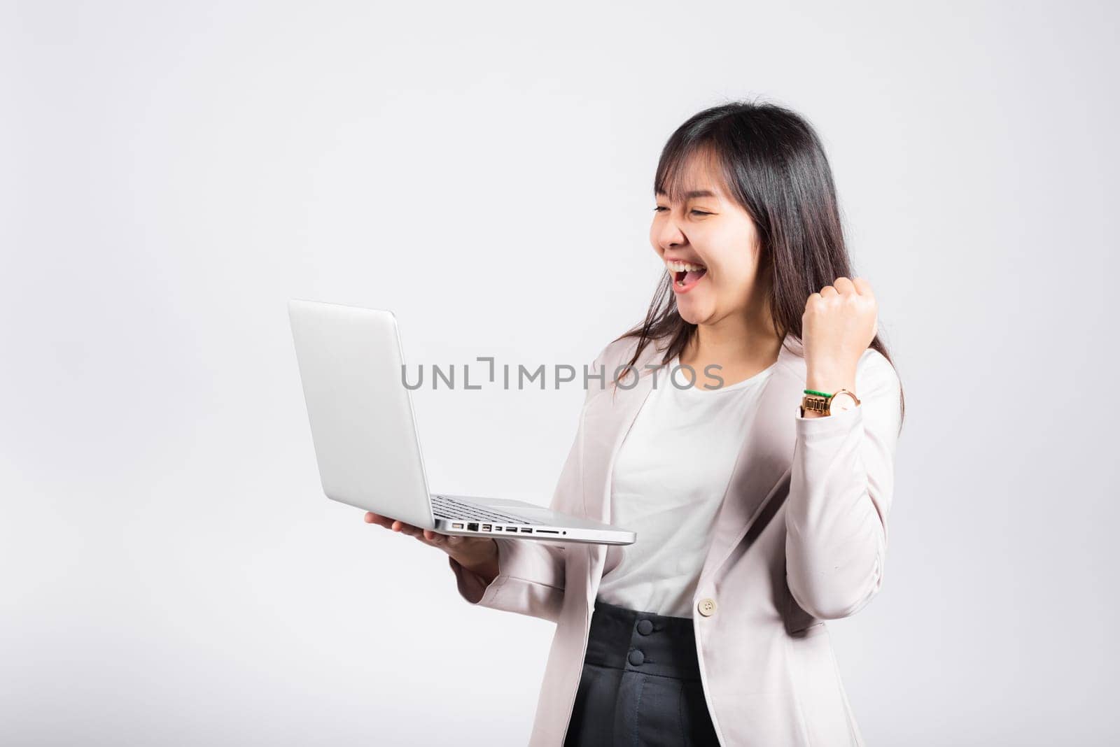 Woman smiling confident holding using laptop computer and excited celebrating success, Portrait excited happy Asian young female person say yes to win studio shot isolated on white background