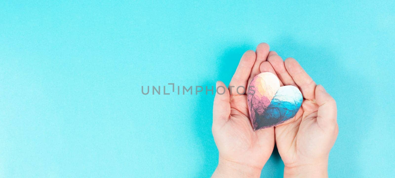 Woman is holding a colorful heart in her hand, love and charity symbol, hope concept, blue background with copy space