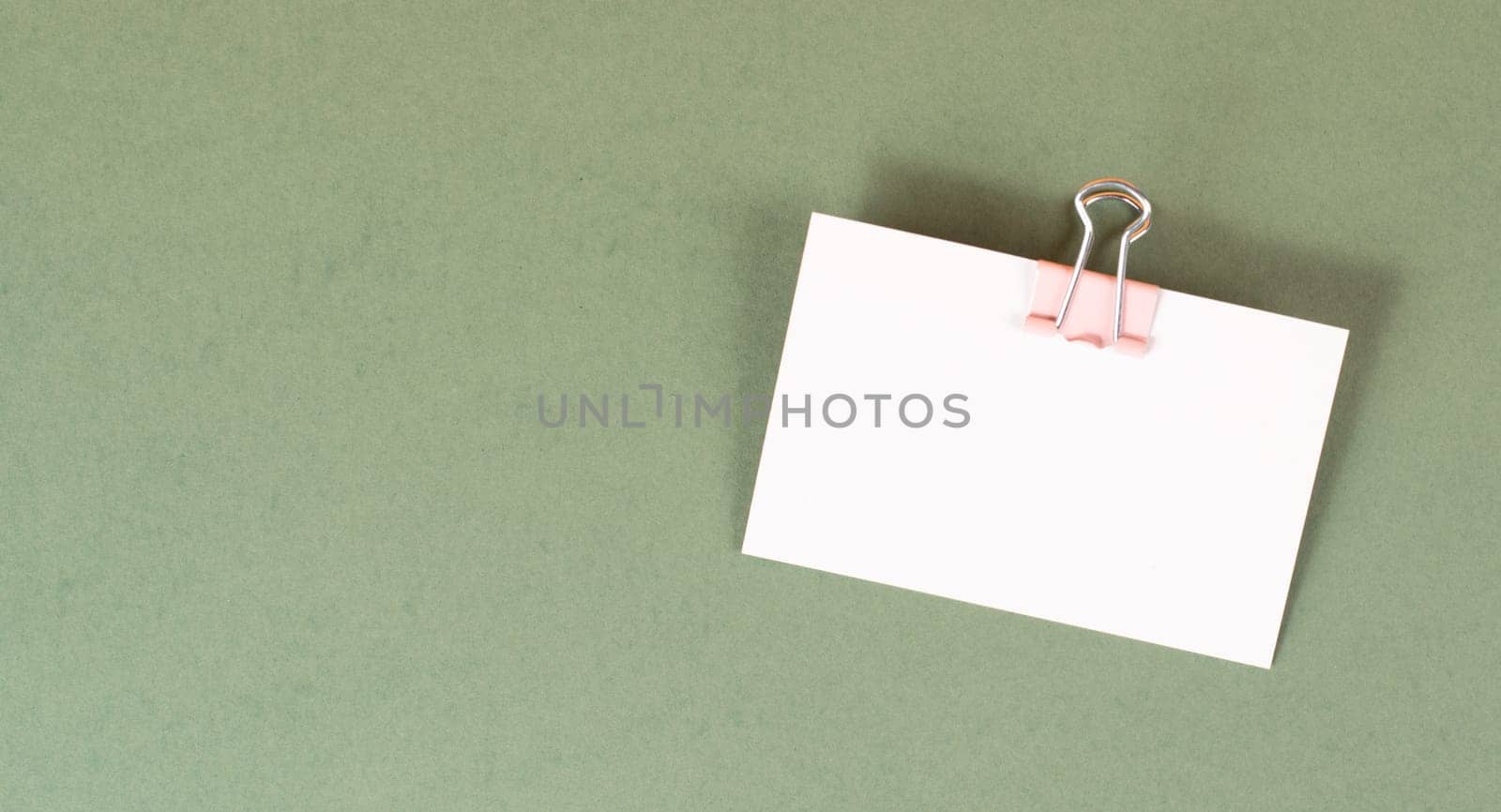 Blank white paper with a paperclip on a green colored background, copy space for text, reminder or message in the office, communication concept