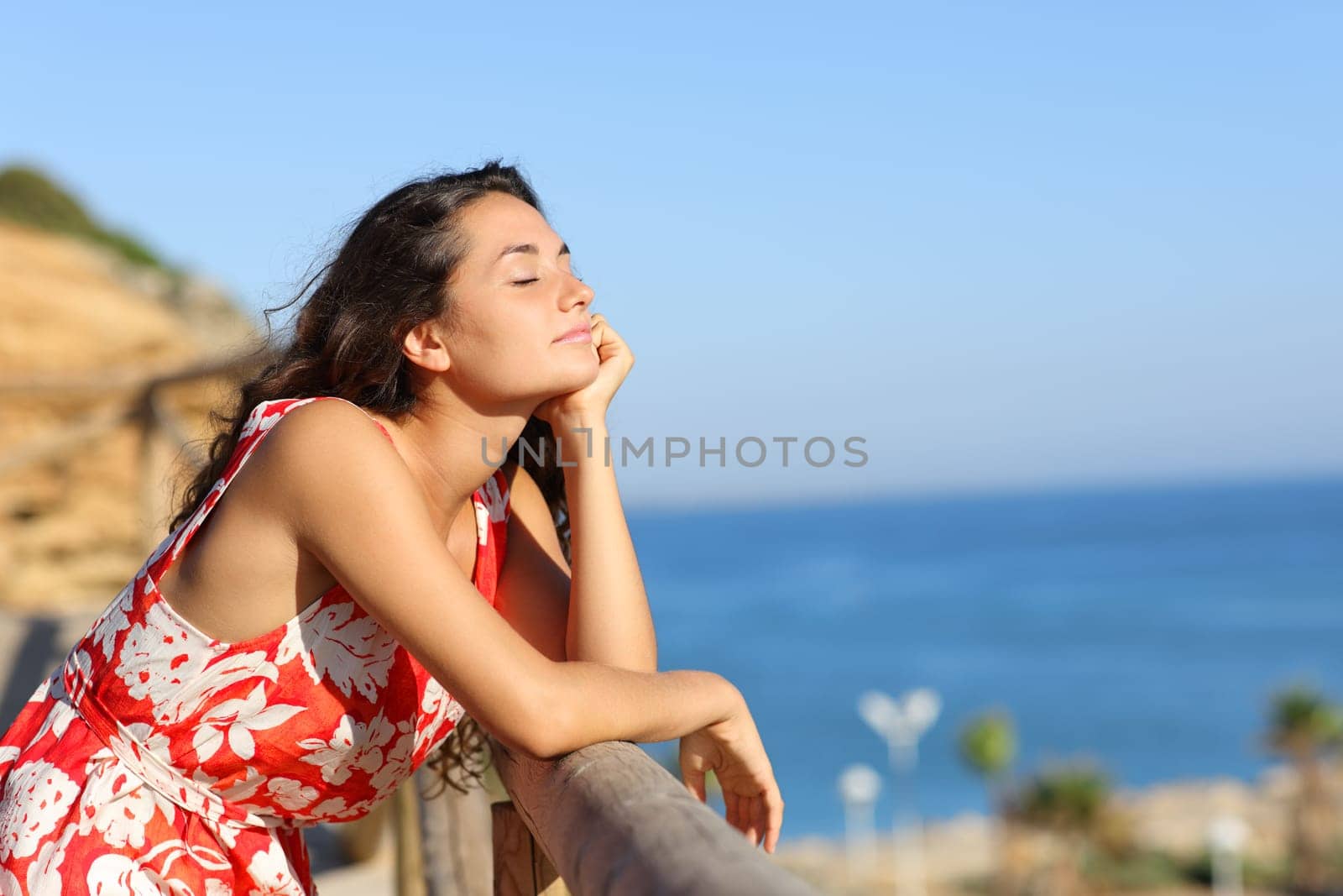 Happy woman in red dress relaxing with eyes closed on the beach