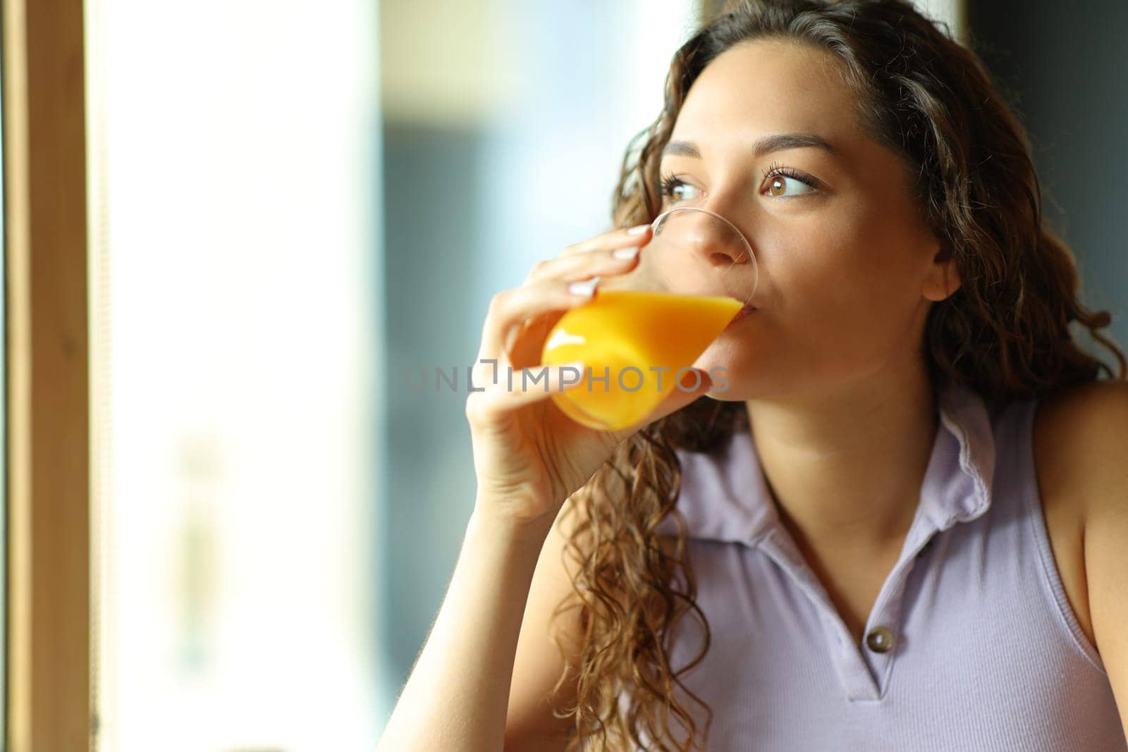 Happy woman drinking orange juice looking through window