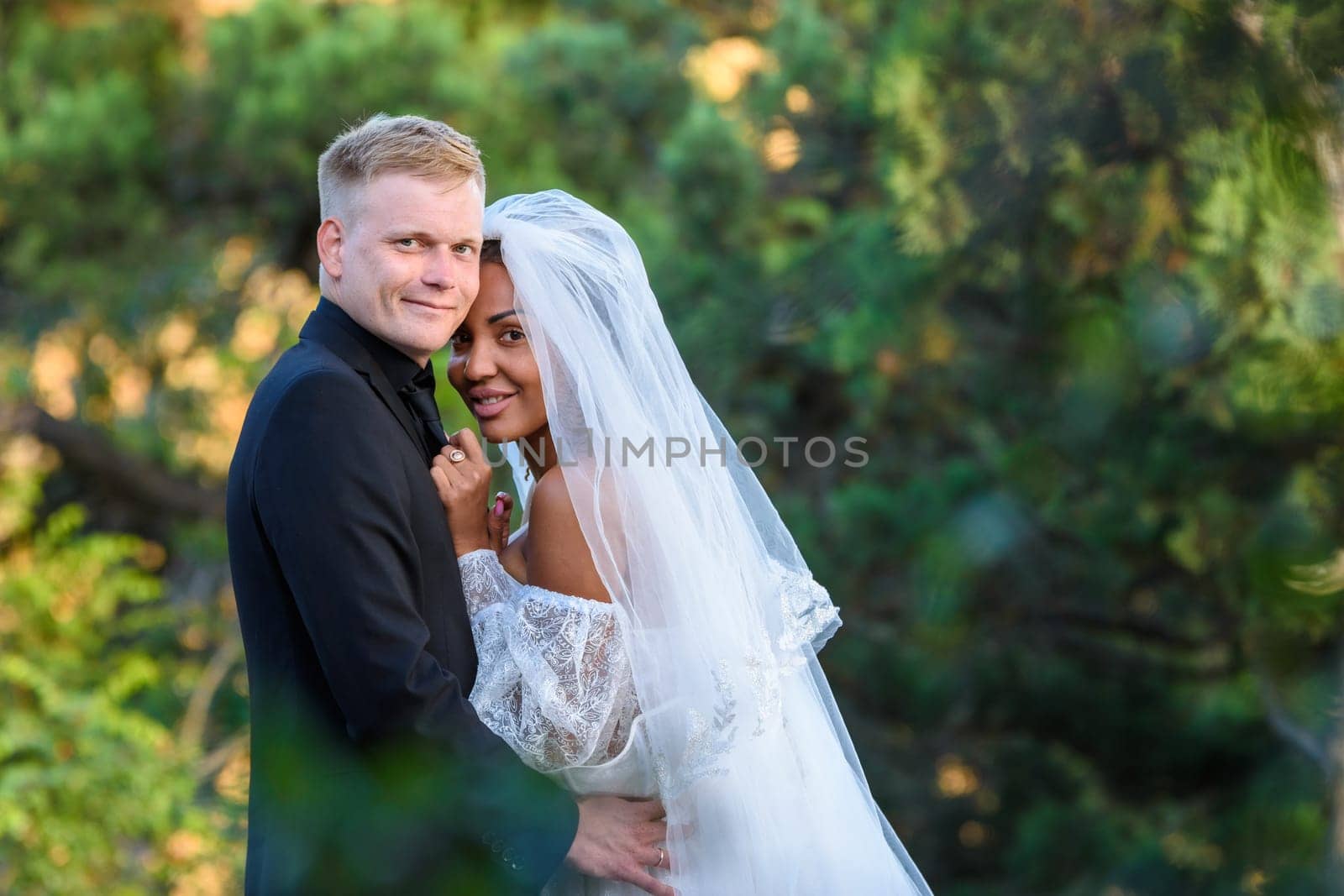 Portrait of young beautiful interracial newlyweds on green foliage background