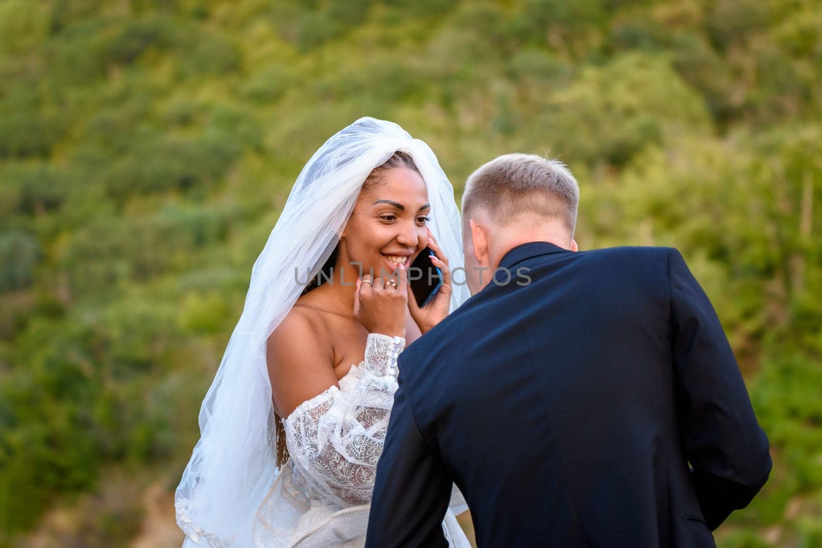 A black bride accepts congratulations on the phone and looks happily at her white husband