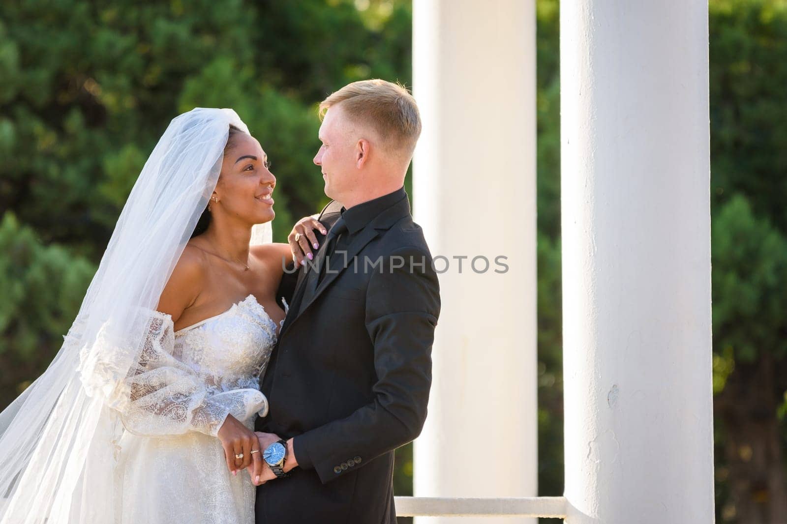 Half-length portrait of mixed-racial newlyweds on a walk against the background of columns and greenery
