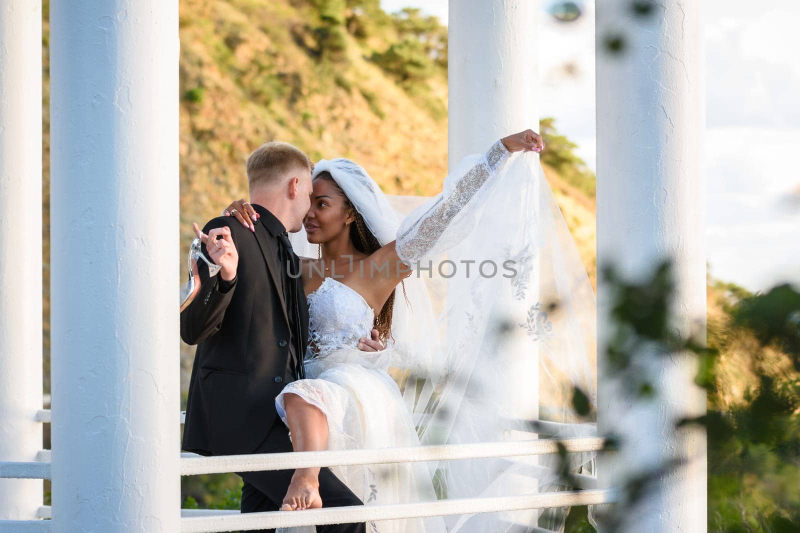 Young beautiful interracial newlyweds hugging in the gazebo
