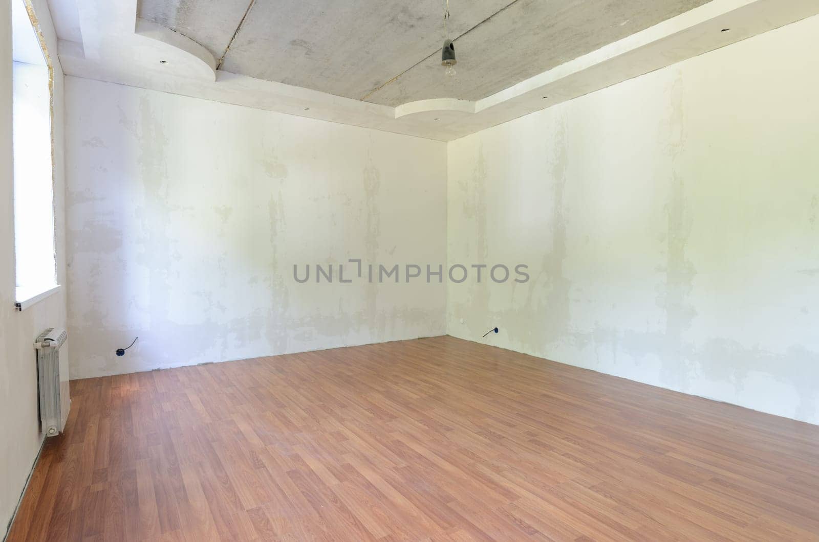 Interior of an empty room during renovation with plastered walls and laminate flooring