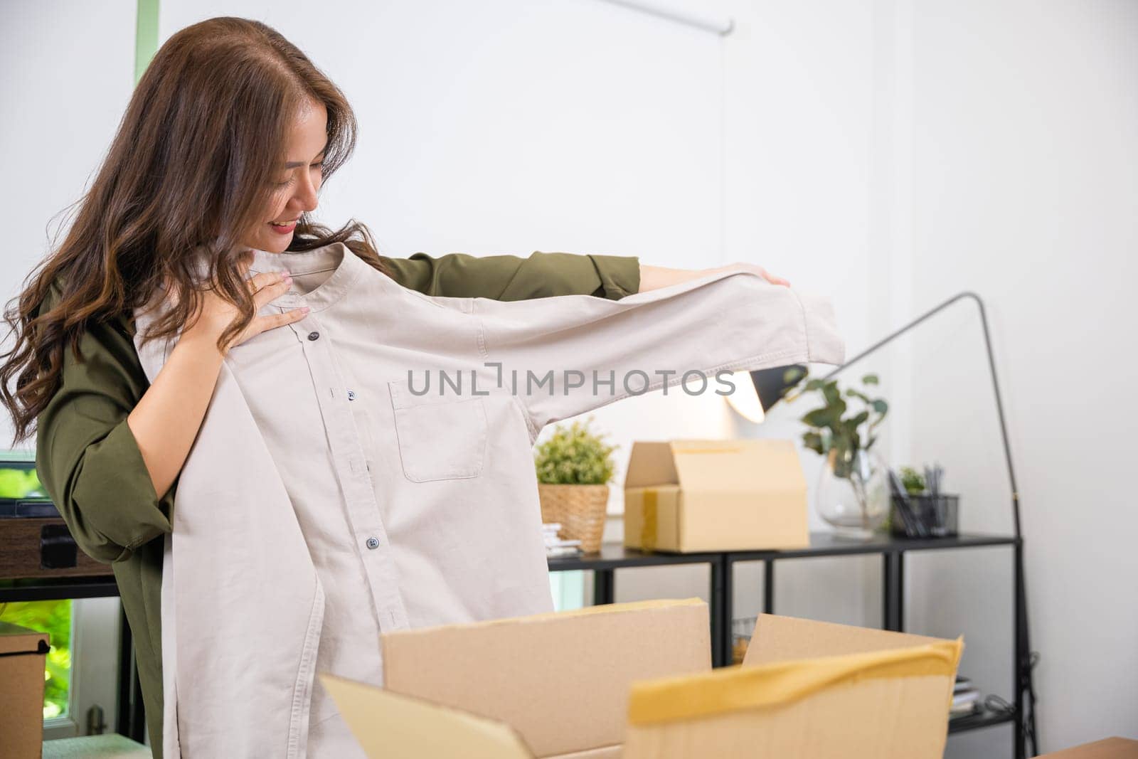Happy Asian woman customer opening box and shirt against body new clothes, Excited smiling female shopper unboxing cardboard box package, shopping online from home, delivery shipping concept