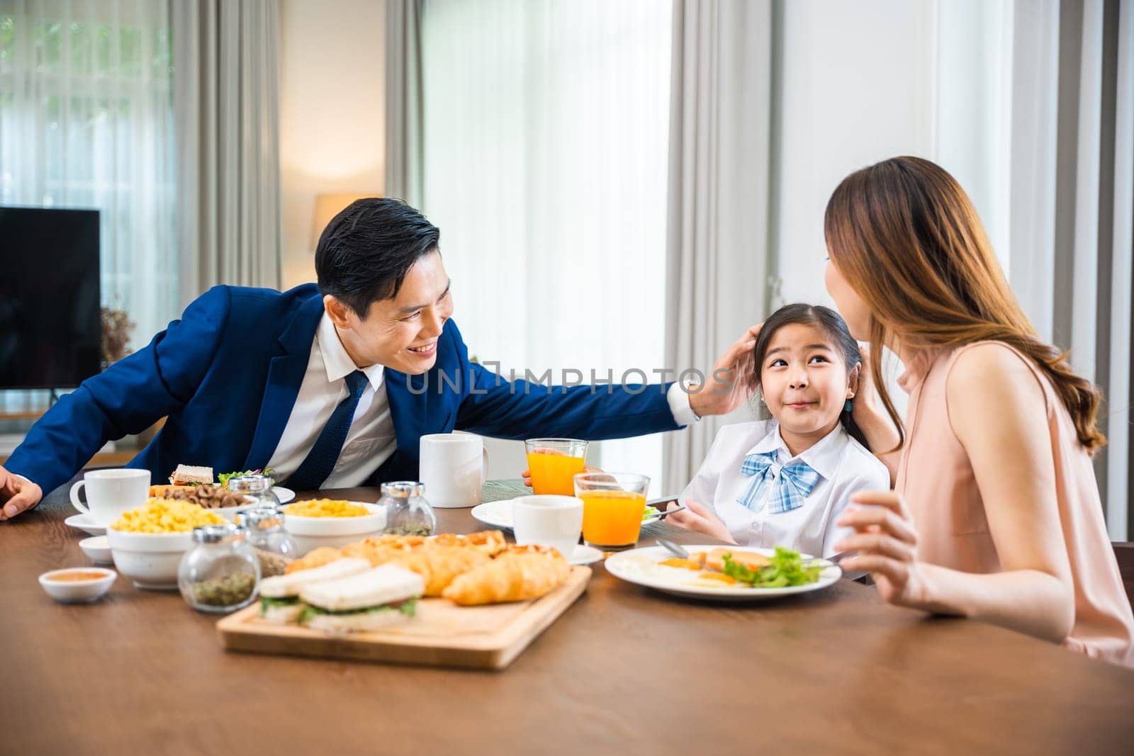 Asian family father, mother with children daughter eating breakfast food on dining table kitchen in mornings together at home before father left for work, happy couple family