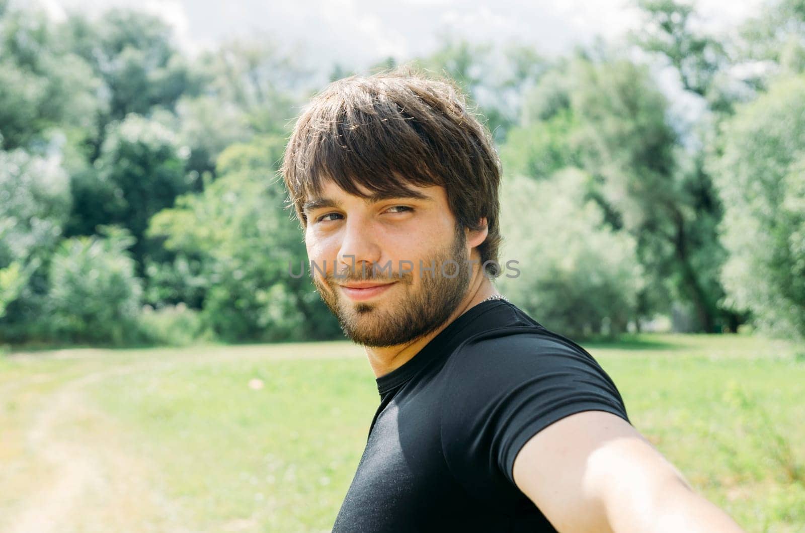 Portrait of young handsome man holding camera and taking outdoor selfie with smartphone. Guy enjoy nature, smiling and looking back in camera.