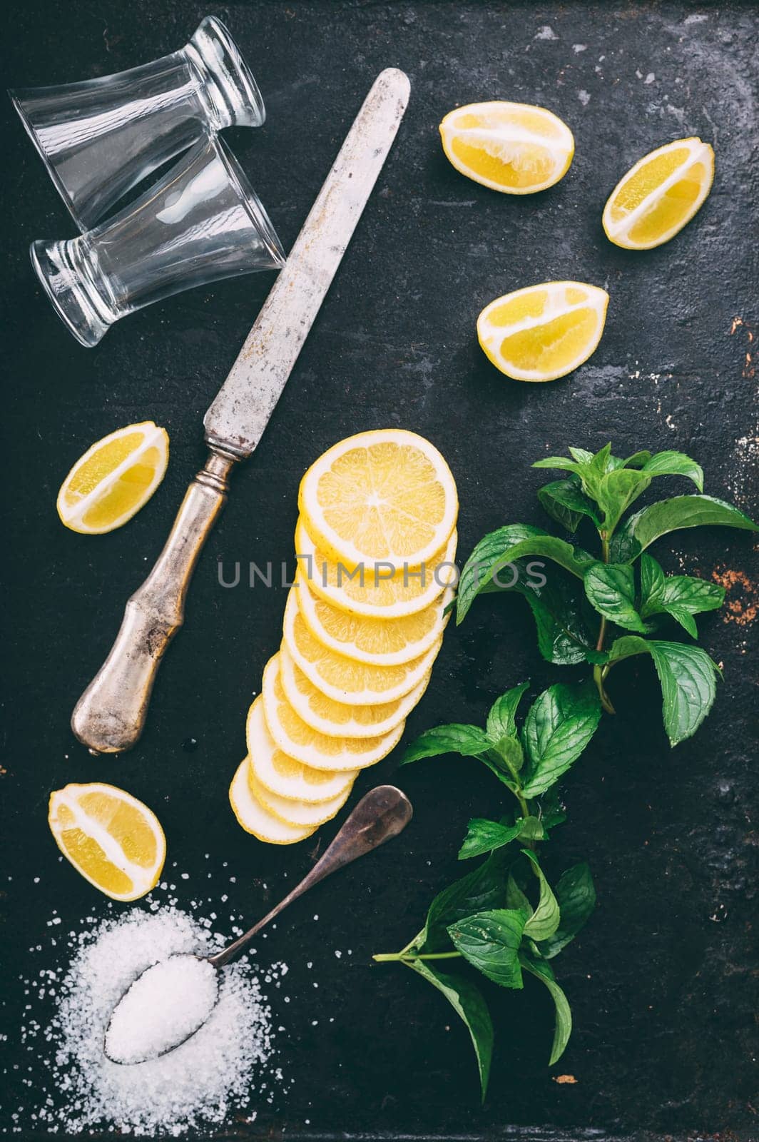 Top view of cocktail ingredients preparation on black rustic background. Tequila shot glasses, lemon slice, salt and mint on grunge dark table form above. Cocktail recipe making.