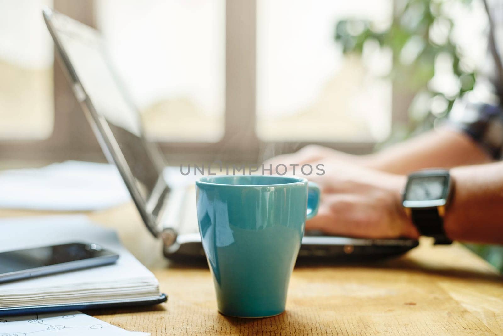 Working desk with laptop, notebook and coffee cup. Closeup of man's hand typing on computer keyboard device. Work space concept.