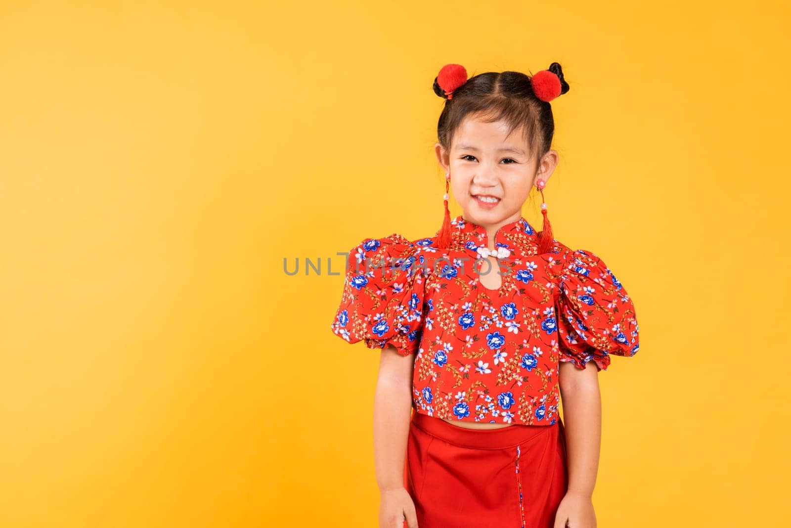 Happy Asian Chinese little girl smile wearing red cheongsam, Portrait children in traditional dress with greeting gesture celebration for Chinese New Year, studio short isolated on yellow background