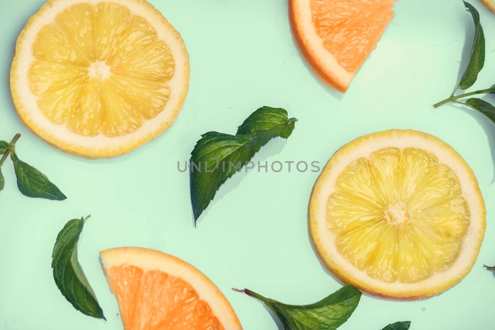 Citrus slices and mint herbs pattern on retro mint background from above. Top view of orange and lemon fruit slices on pastel background.