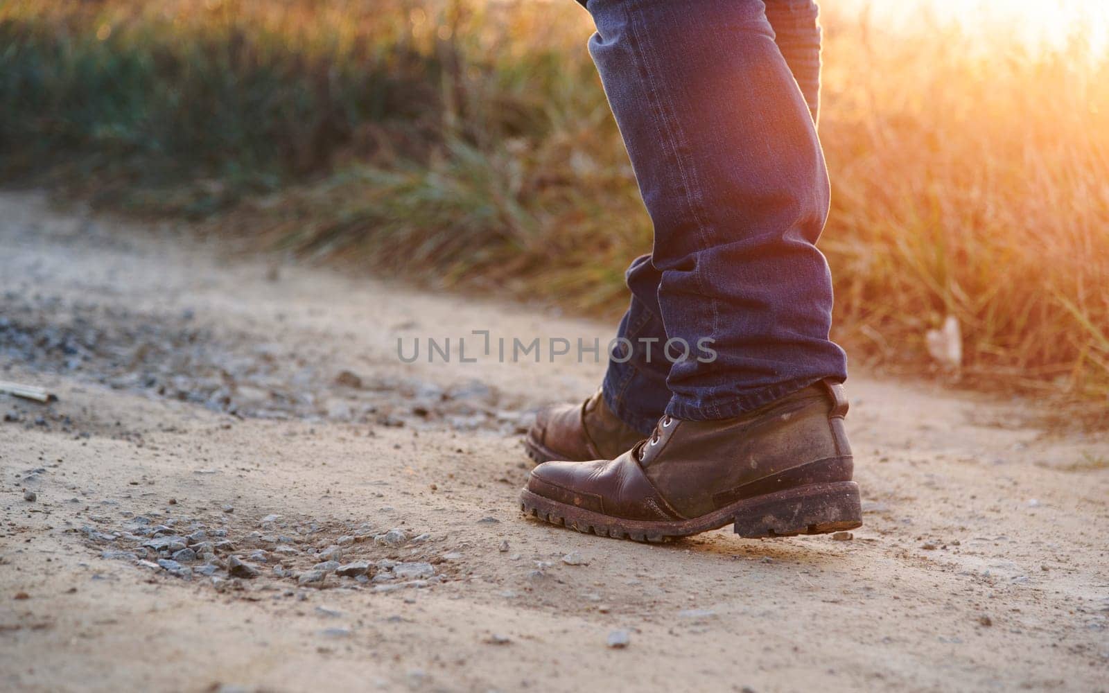 Closeup of man in hiking shoes walking on rural path in the mountain at sunset
