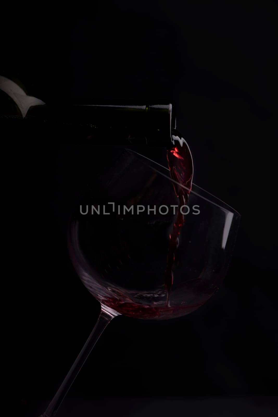 Red wine pouring in wineglass from bottle over black background. Wine list design menu with copyspace. Alcohol beverage card backdrop.