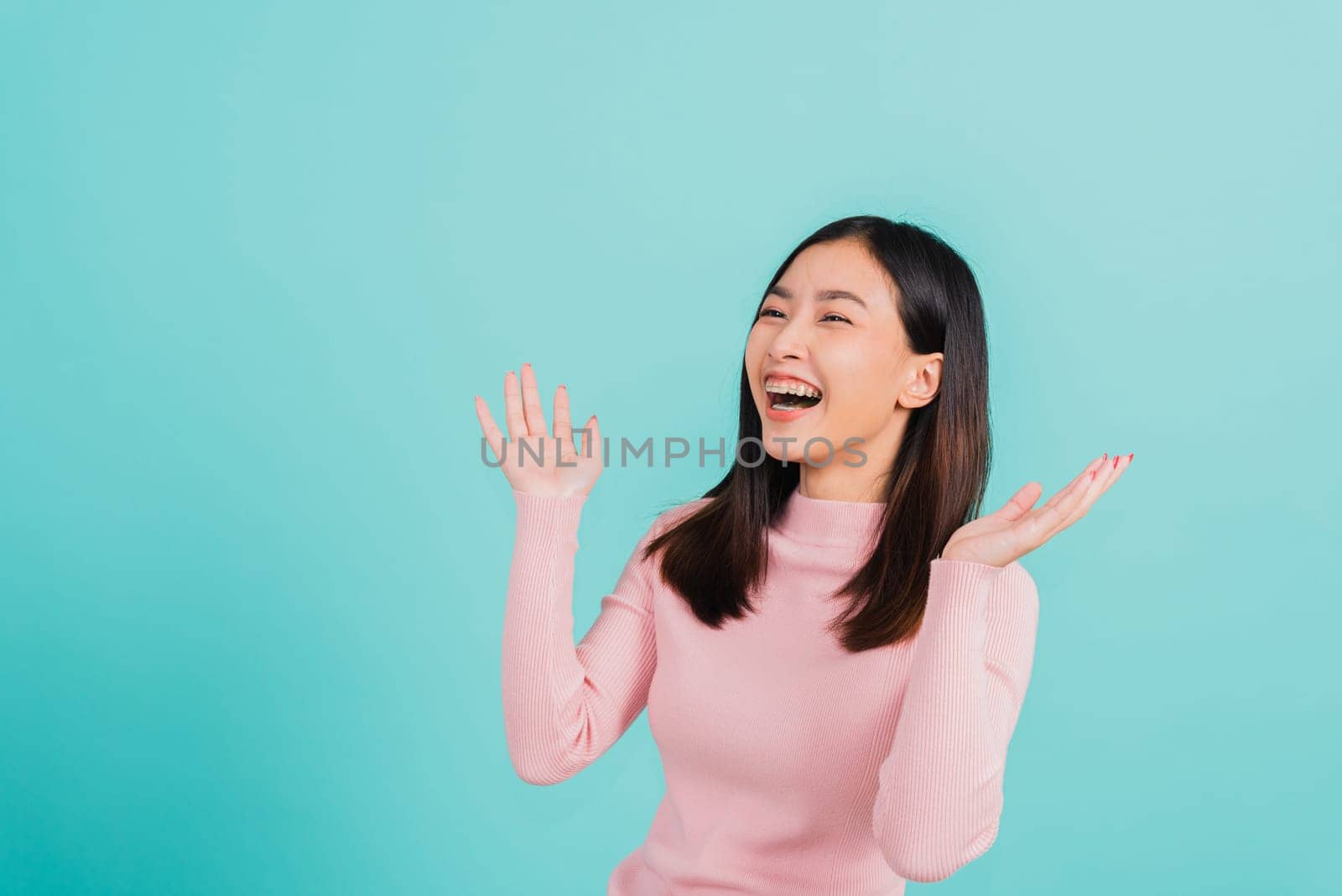 Happy young Asian beautiful woman smiling wear silicone orthodontic retainers on teeth surprised she is excited screaming and raise hand make gestures wow, studio shot isolated on blue background