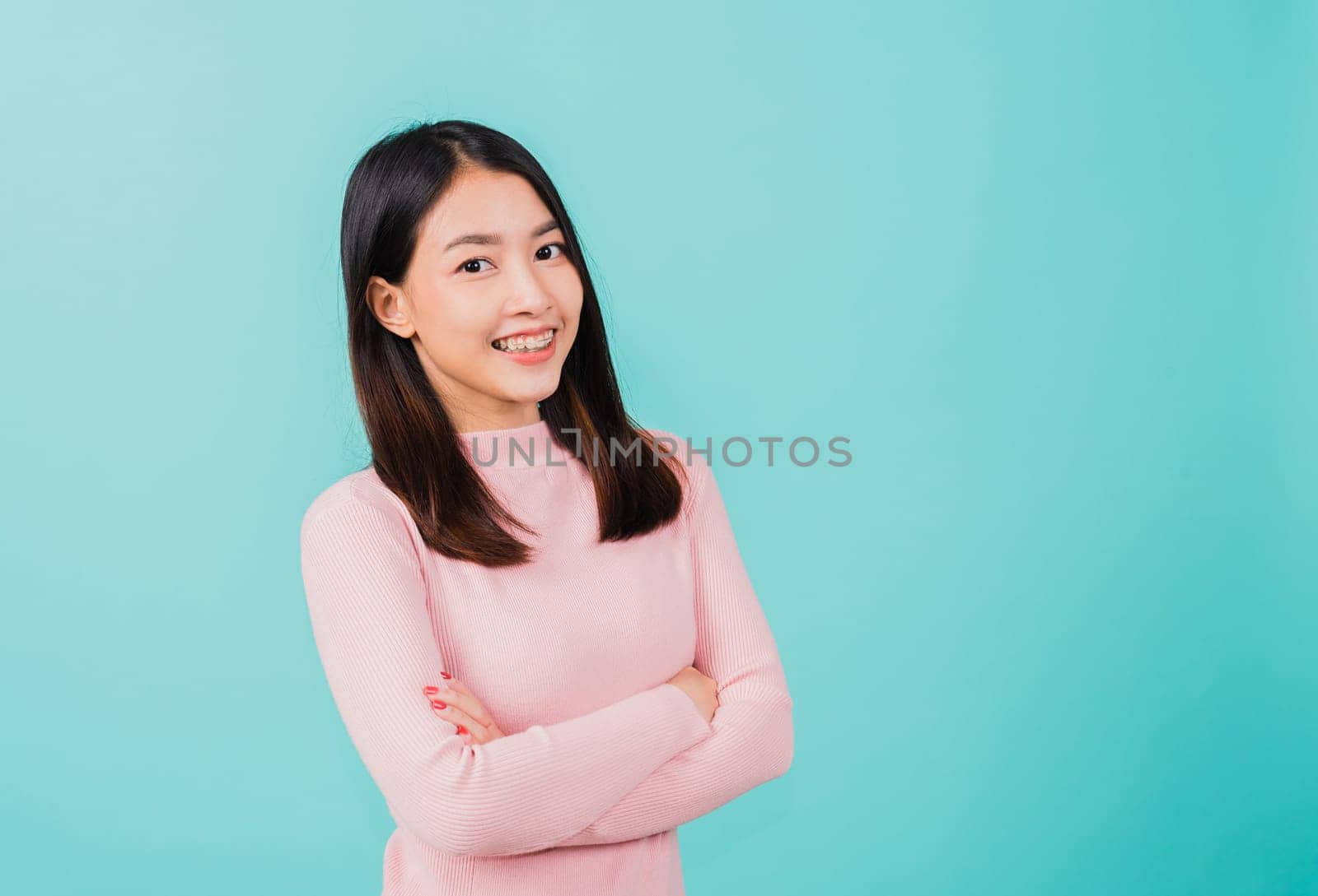 Young Asian beautiful woman smiling wear silicone orthodontic retainers on teeth with crossed arms, studio isolated on blue background, retaining tools after removable braces. Dental hygiene concept