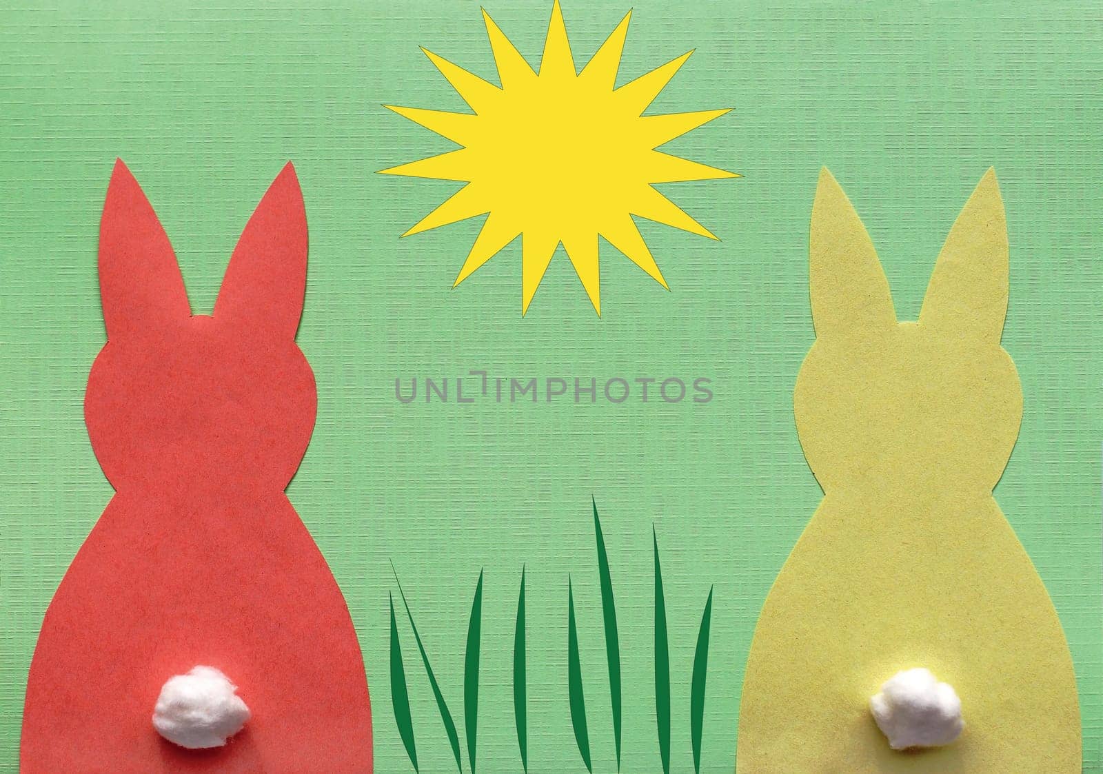 One red and one yellow paper bunny on green background with illustrated sun and grass