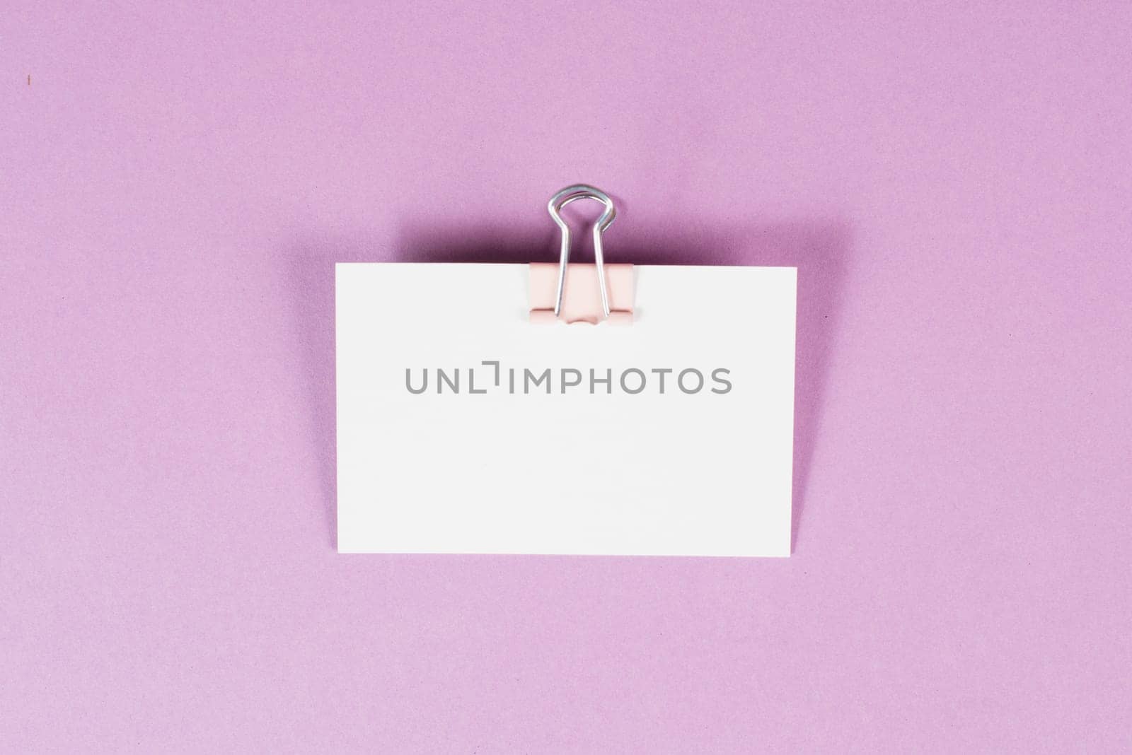 Blank white paper with a paperclip on a pink colored background, copy space for text, reminder or message in the office, communication concept