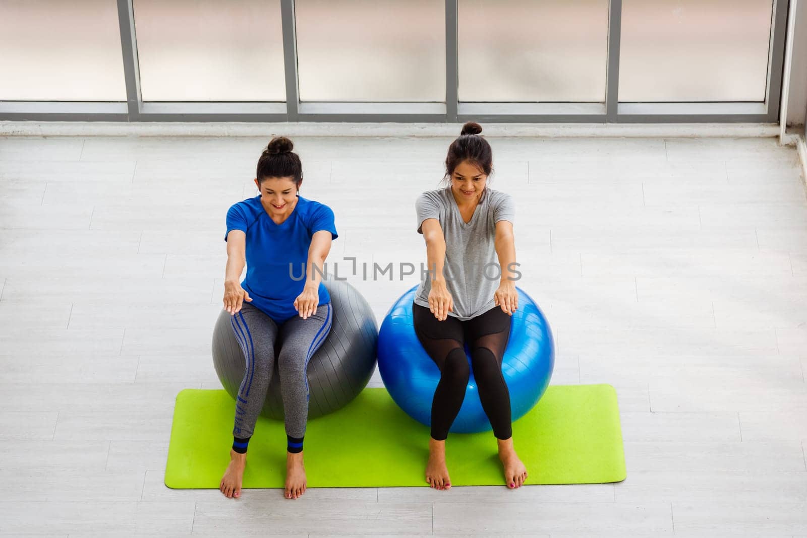 Above two Asian adult and young woman in sportswear doing aerobics yoga exercise with sitting on fitness ball indoor yoga studio, fit sport healthy workout lifestyle exercise