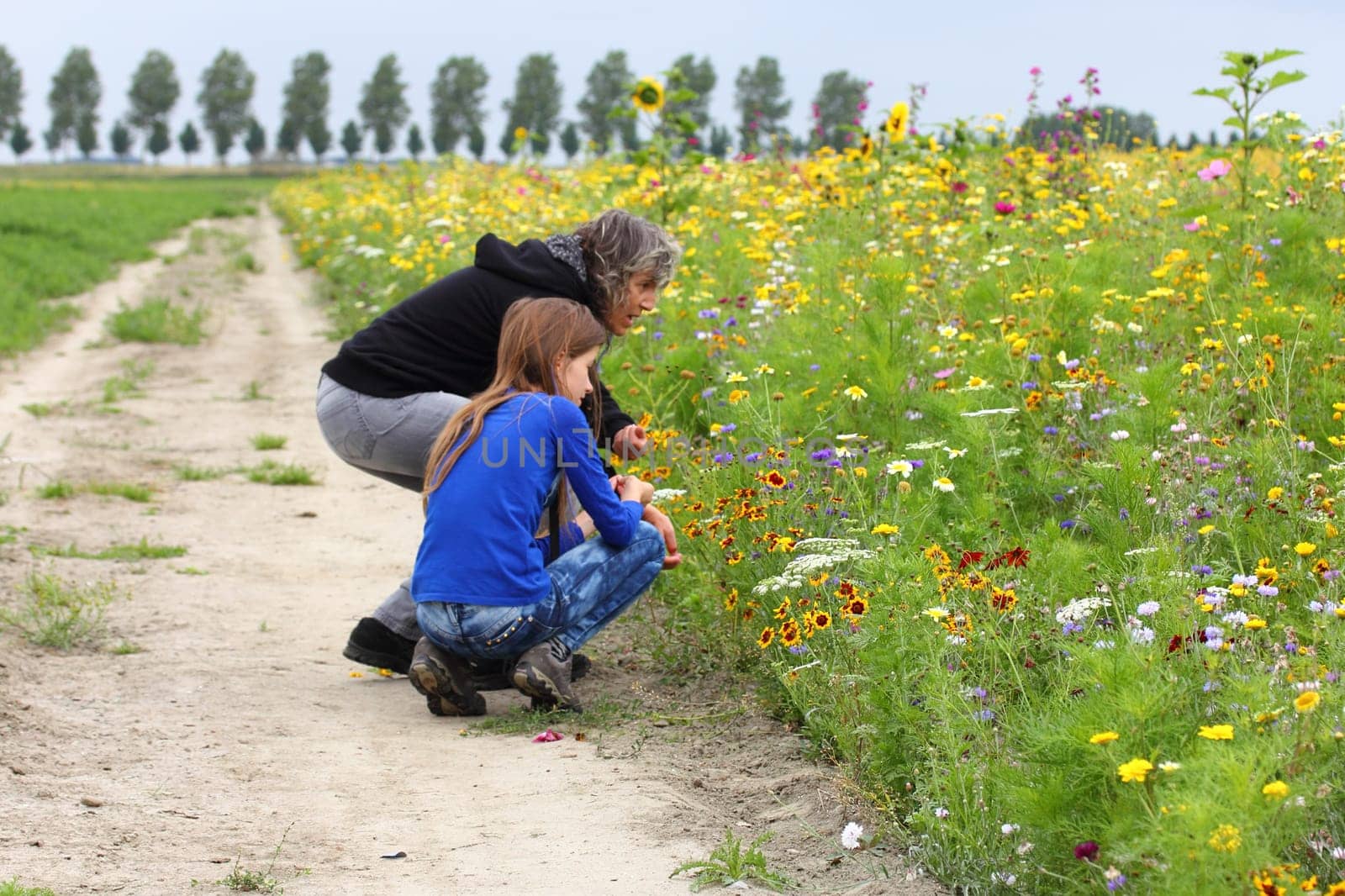 Mother and daughter admire a beautiful flower bed with colourful perennials and blooming flowers.