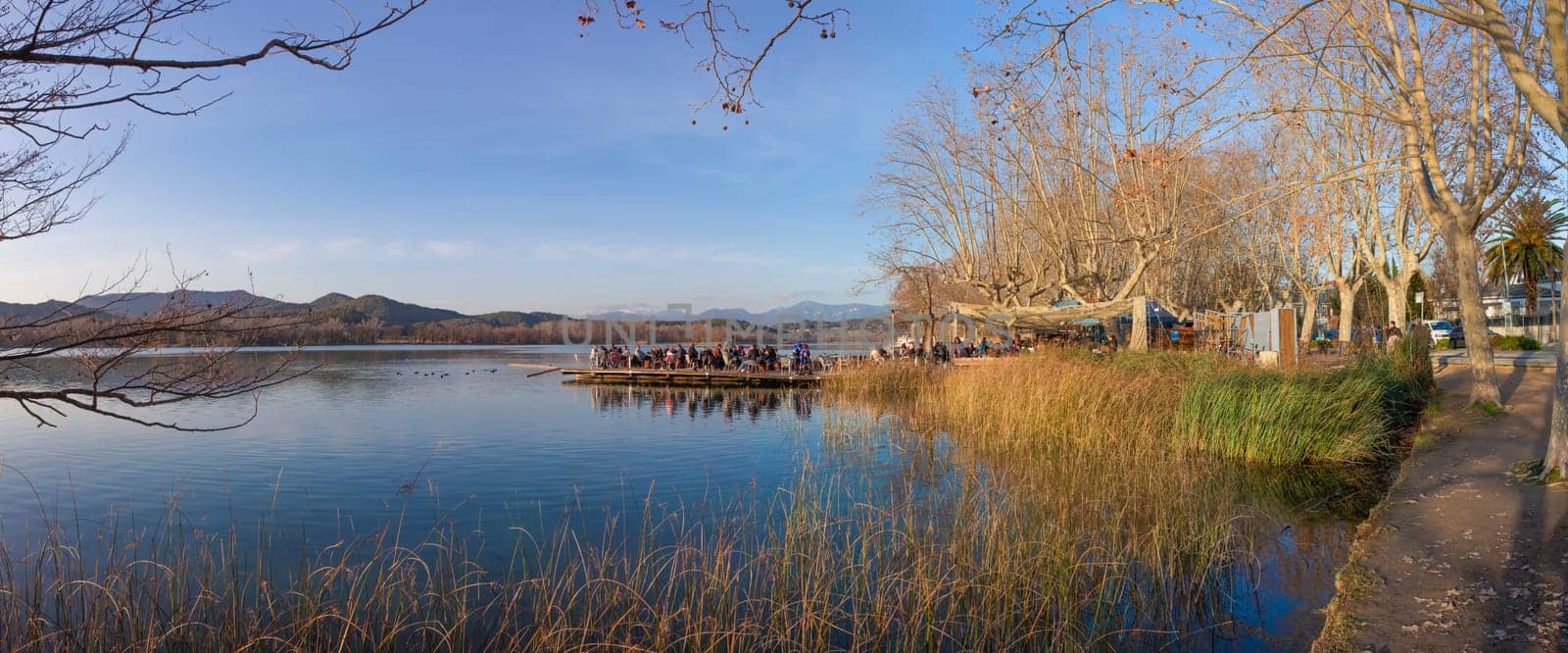 People enjoying the winter sun over pier restaurant at Lake of Banyoles, Girona, Catalonia, Spain