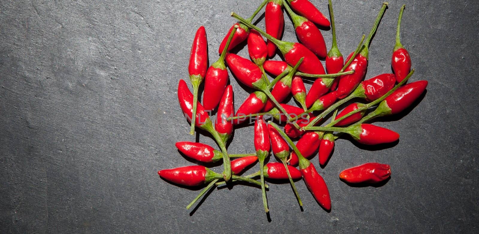 Black slate with piri-piri chili pepper. Studio shot with natural light. Wooden background