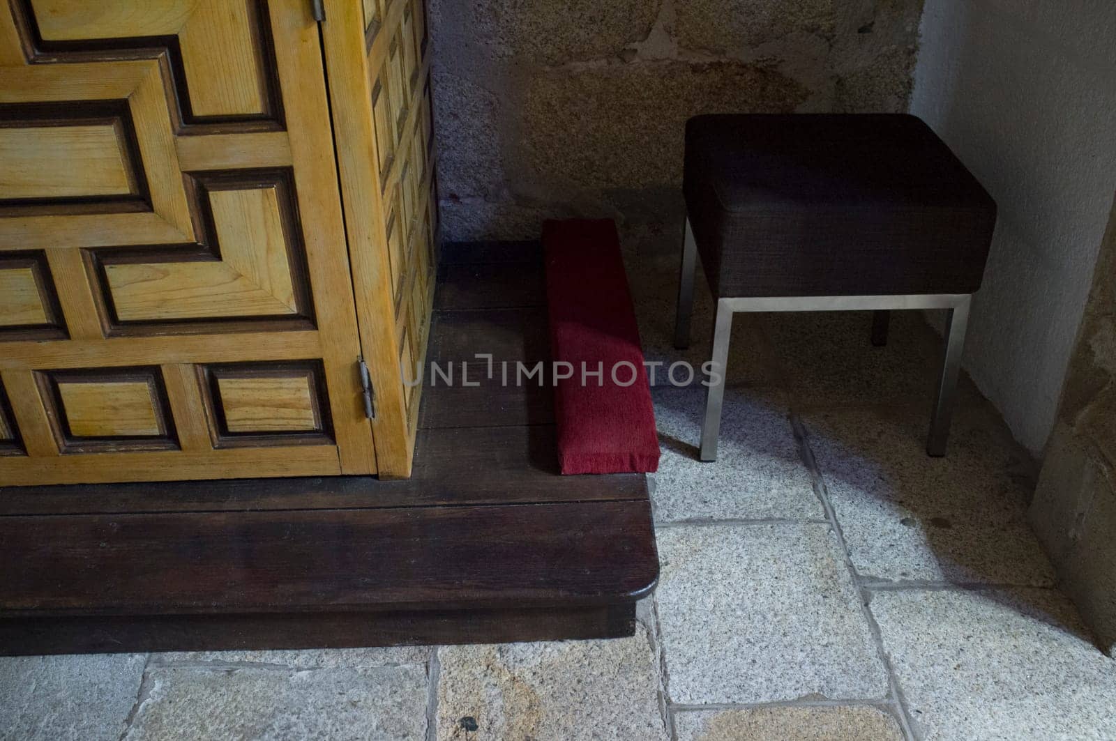 Wooden confessional foot with bench and prie-dieu cushion. Selective focus