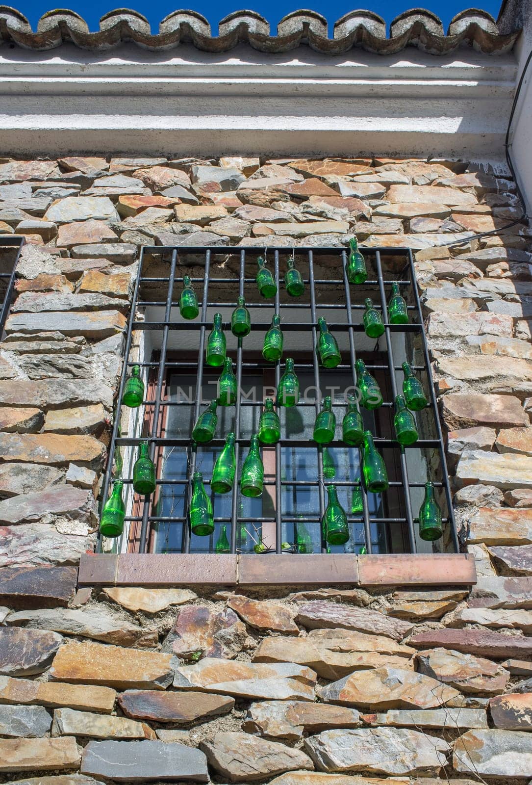 Rural residence house window decorared with hanging green glass bottles. Low angle view