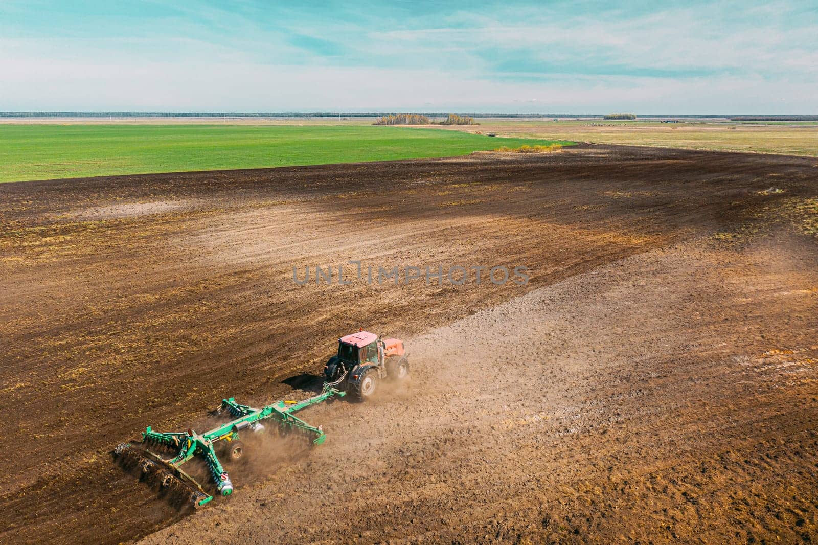 Aerial View. Tractor Plowing Field. Beginning Of Agricultural Spring Season. Cultivator Pulled By A Tractor In Countryside Rural Field Landscape. Dust Rises From Under Plows.
