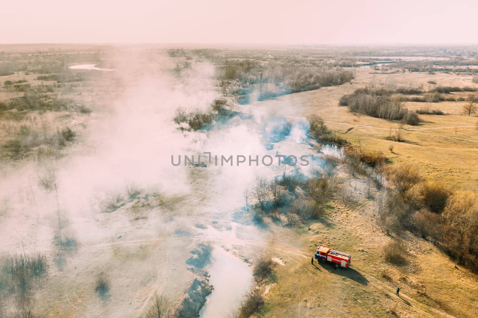 Aerial View. Spring Dry Grass Burns During Drought Hot Weather. Bush Fire And Smoke. Fire Engine, Fire Truck On Firefighting Operation. Wild Open Fire Destroys Grass. Ecological Problem Air Pollution.