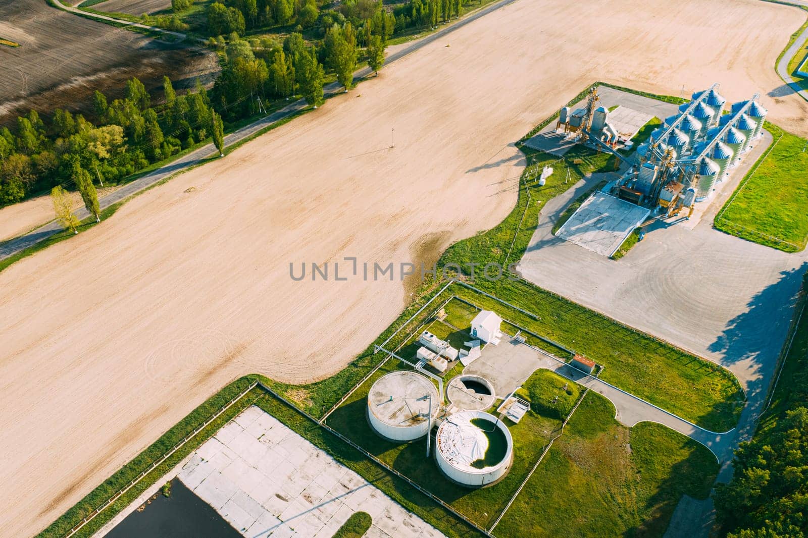 Biogas Bio-gas Plant From Pig Farm And Granary, Grain-drying Complex, Commercial Grain Or Seed Silos In Sunny Spring Rural Landscape. Corn Dryer Silos, Inland Grain Terminal, Elevators.
