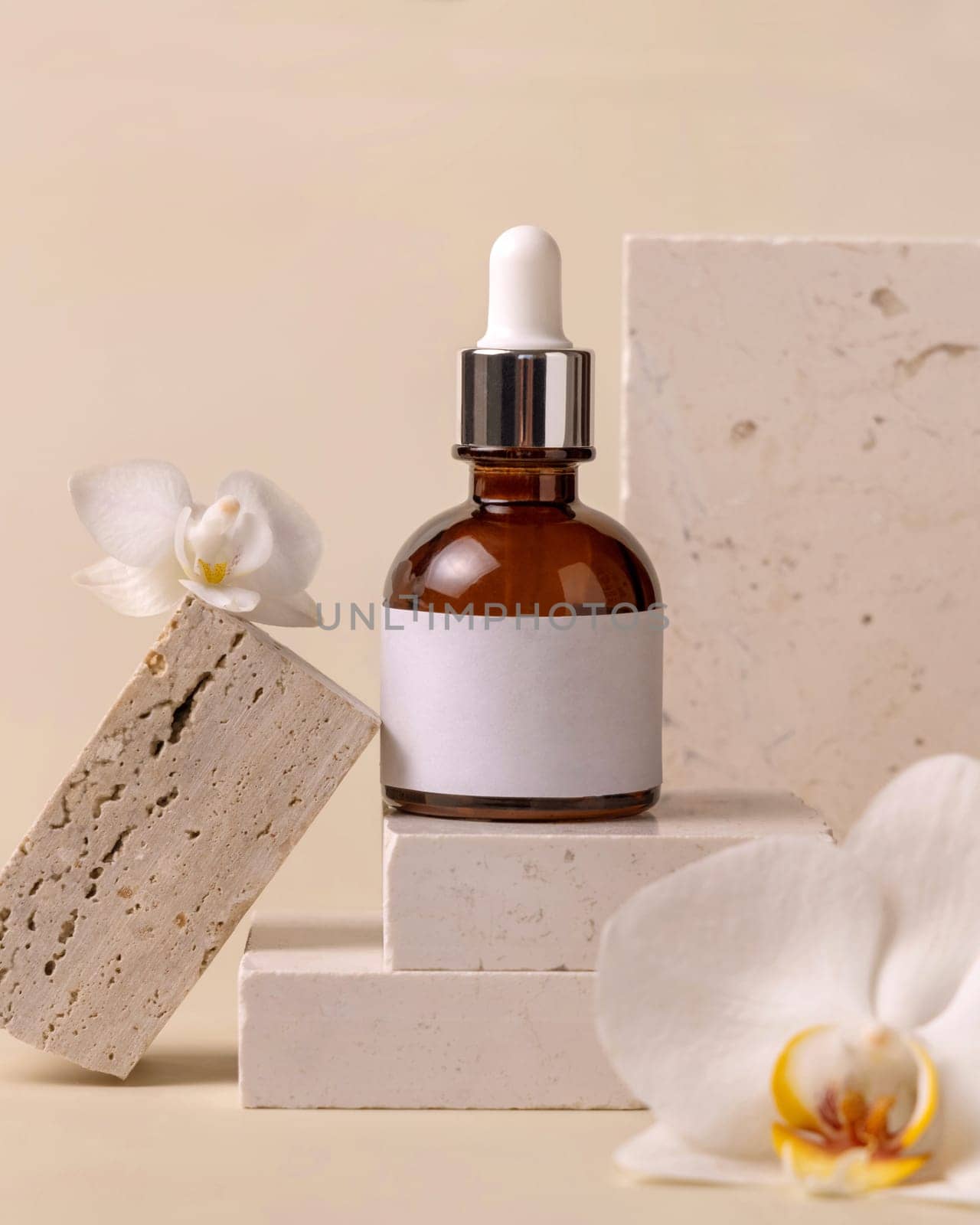 Brown Glass Dropper bottle on stone near white orchid flowers on light yellow close up, label mockup. Skincare handmade beauty product, serum or lotion. Exotic natural cosmetics..