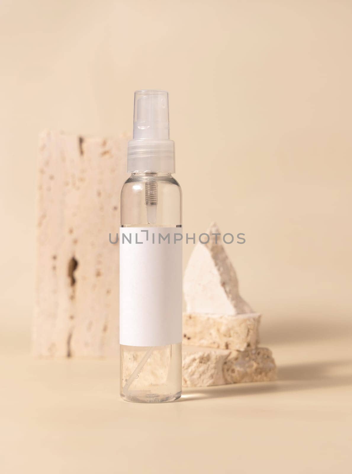 Spray bottle with blank label near stones on light beige close up, packaging mockup. Skincare beauty product, lotion or cleanser. Natural cosmetics, minimal composition..