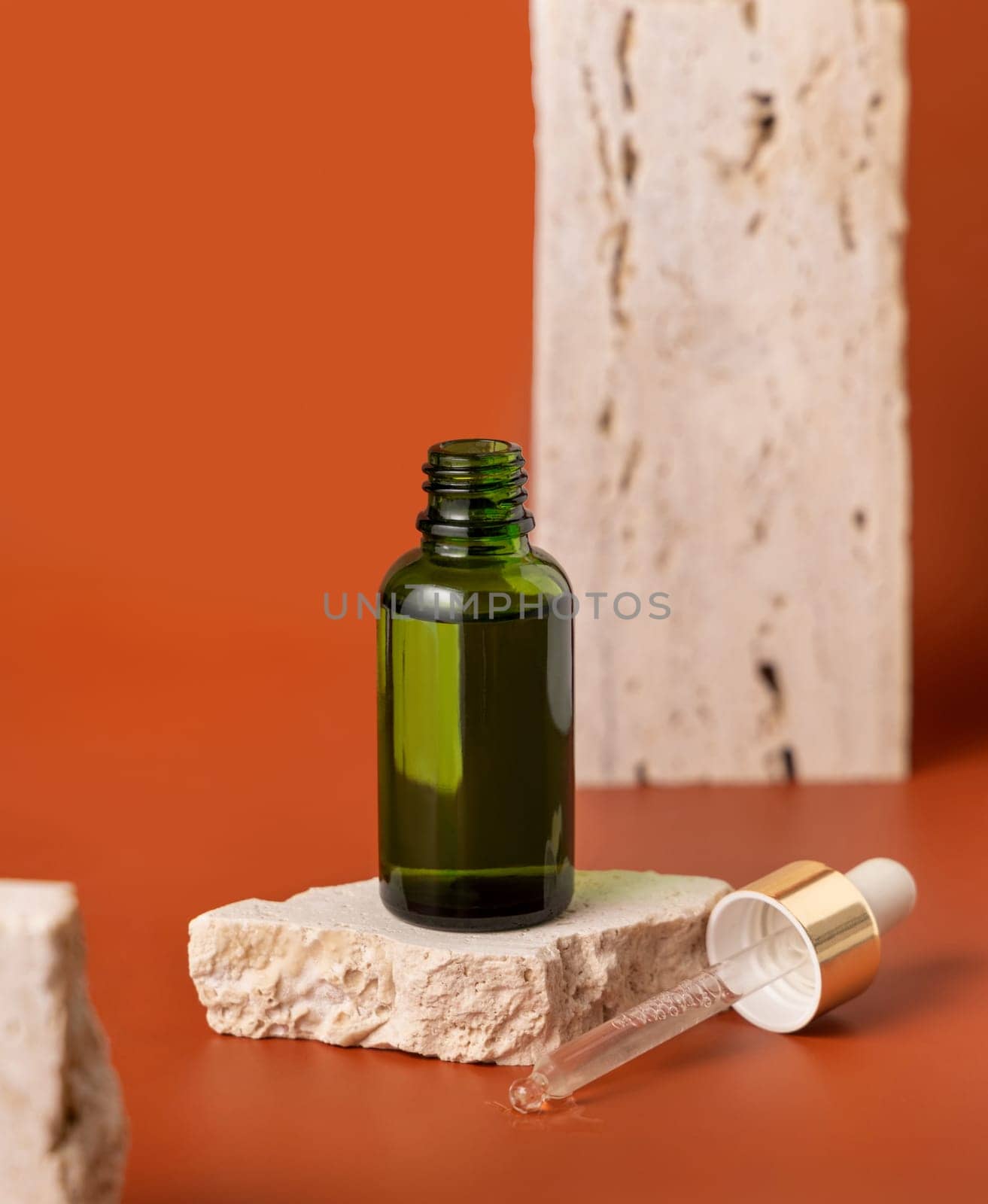 Opened Green dropper bottle on beige stone on red close up, cosmetic Mockup. Skincare beauty product, serum or essential oil. Natural cosmetics..