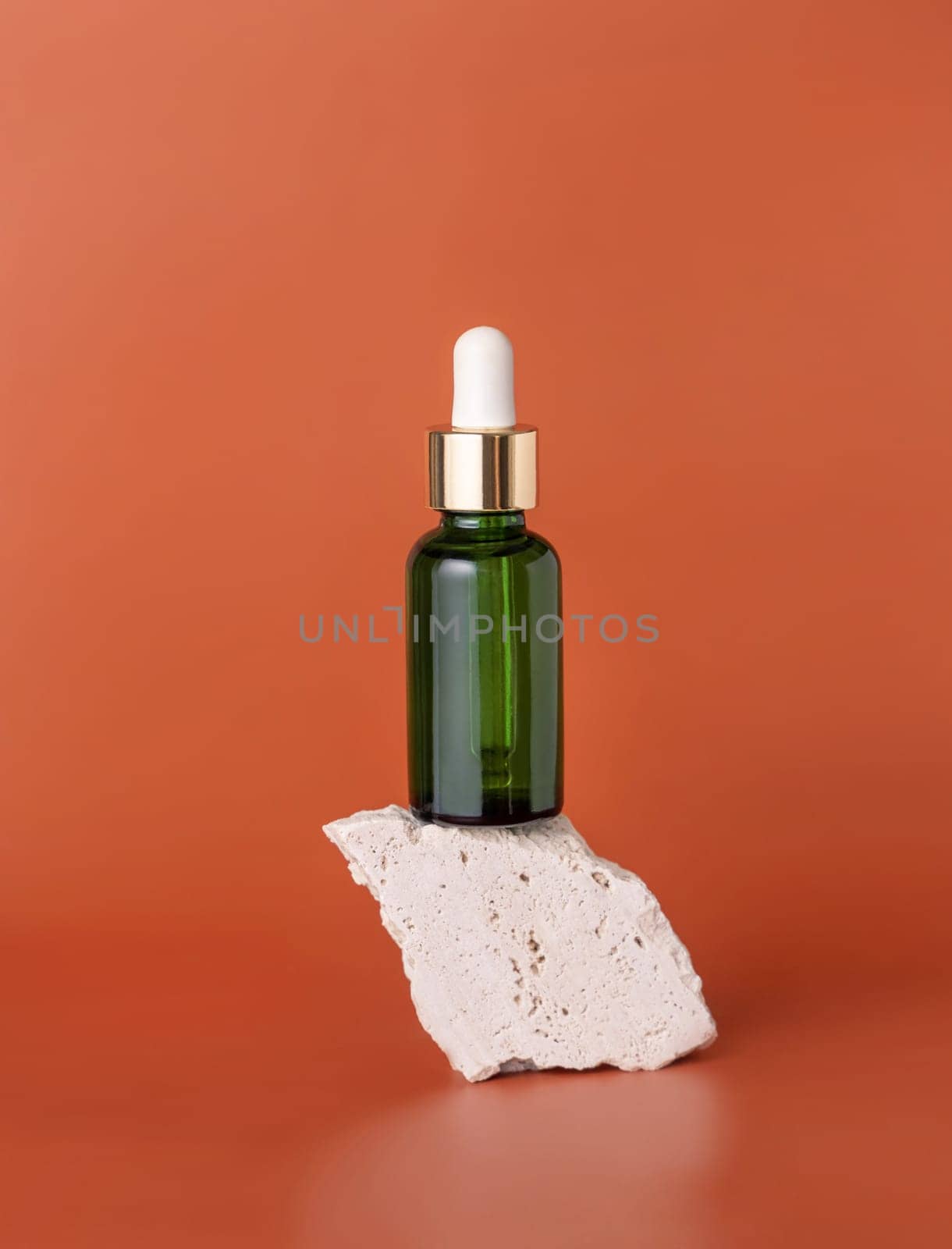 Green dropper bottle on beige stone on red close up, cosmetic Mockup. Skincare beauty product, serum or essential oil. Natural cosmetics..