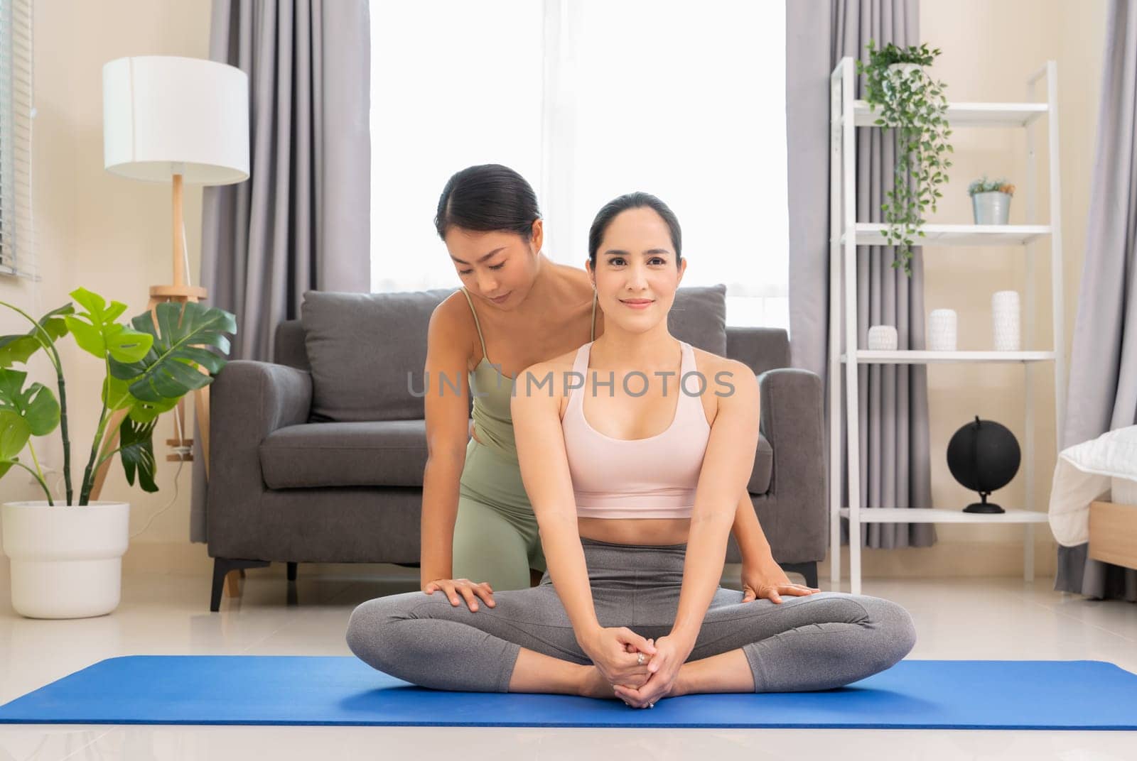 Young woman beginning yoga practice with private teacher at home. Professional instructor teaches student to do Baddha Konasana exercise or Butterfly pose, stretching exercises for inner thighs and hip. Healthy lifestyle concept