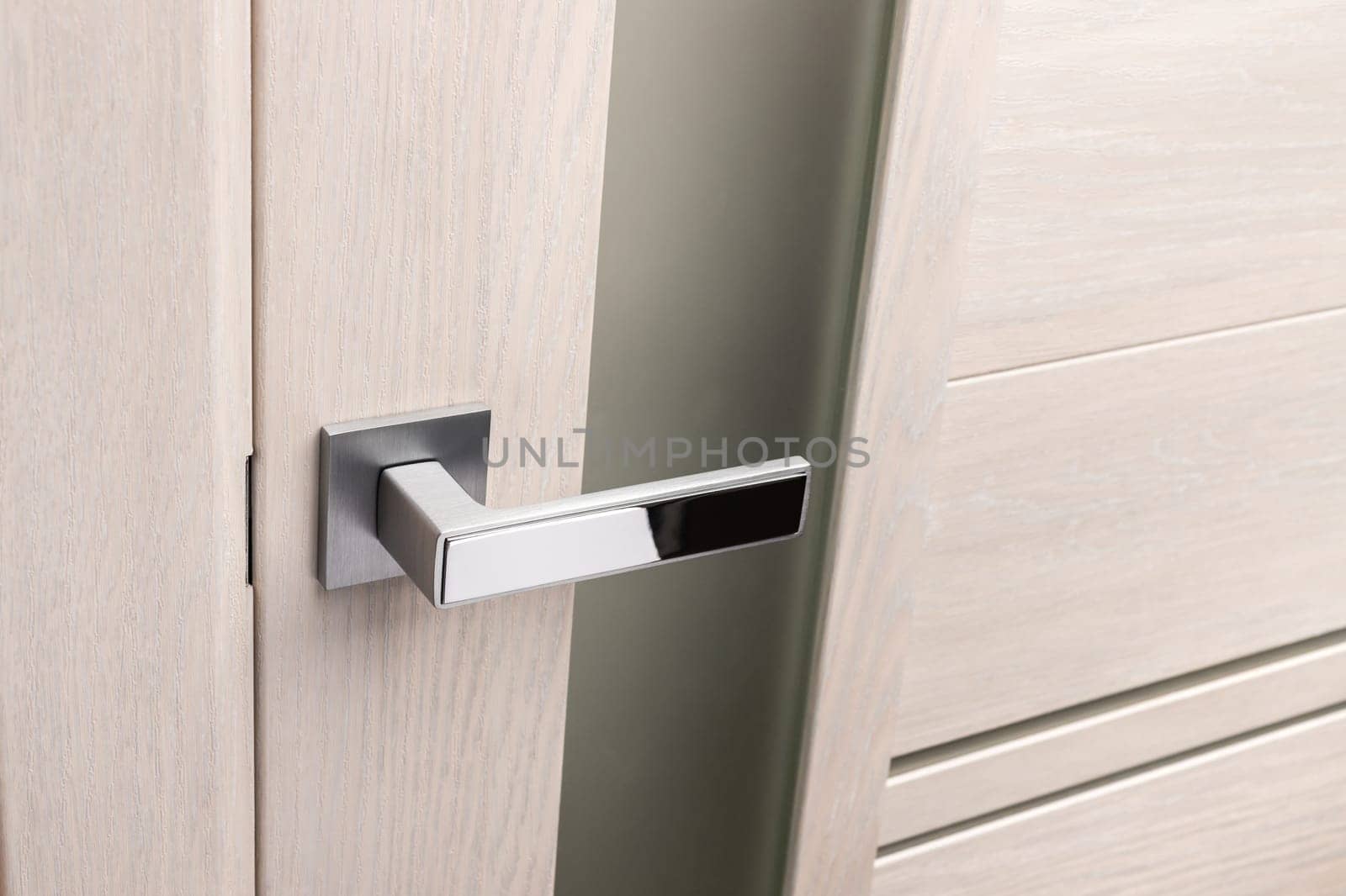 Close up of beautiful and stylish new metal door knob on modern interior door. Silver chrome handle on light beige door with frosted glass. Concept of interior details.