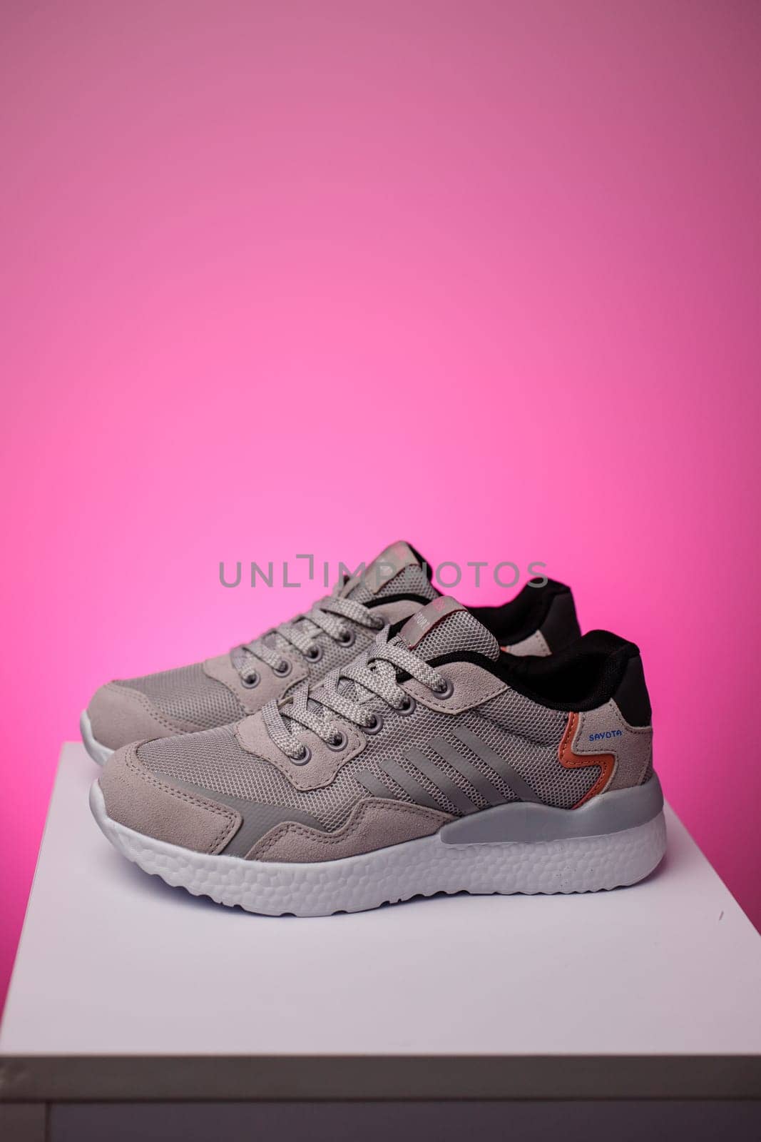 Gray running shoes. Pair of sports shoes standing on white podium on pink background. Side view of gray sneakers on white sole. Sports shoes advertising concept.