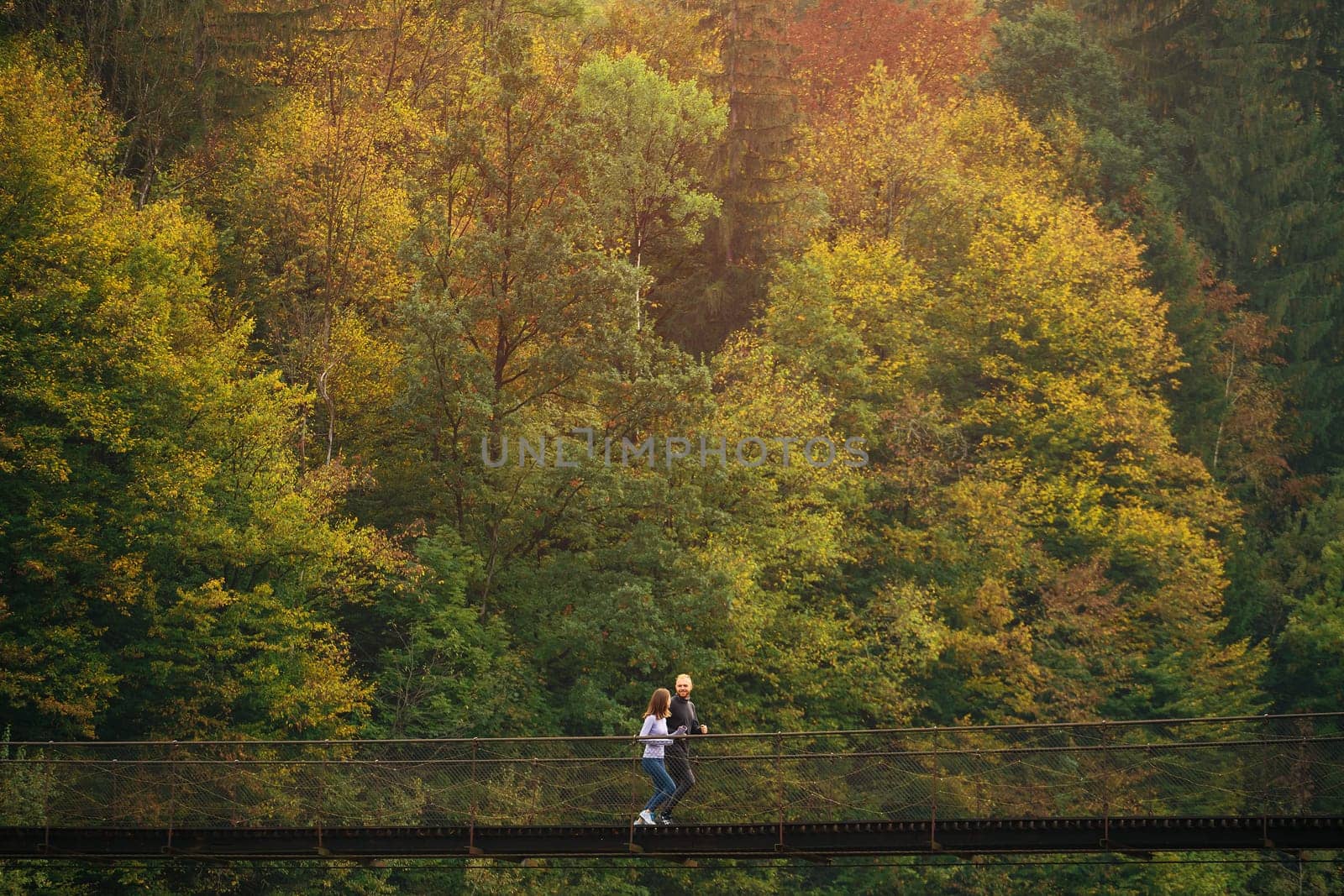 Early morning workout. Young sports family performs a morning jog on a suspension bridge against the backdrop of a mountain forest. Concept of active and healthy lifestyle. Mountain forest landscape.
