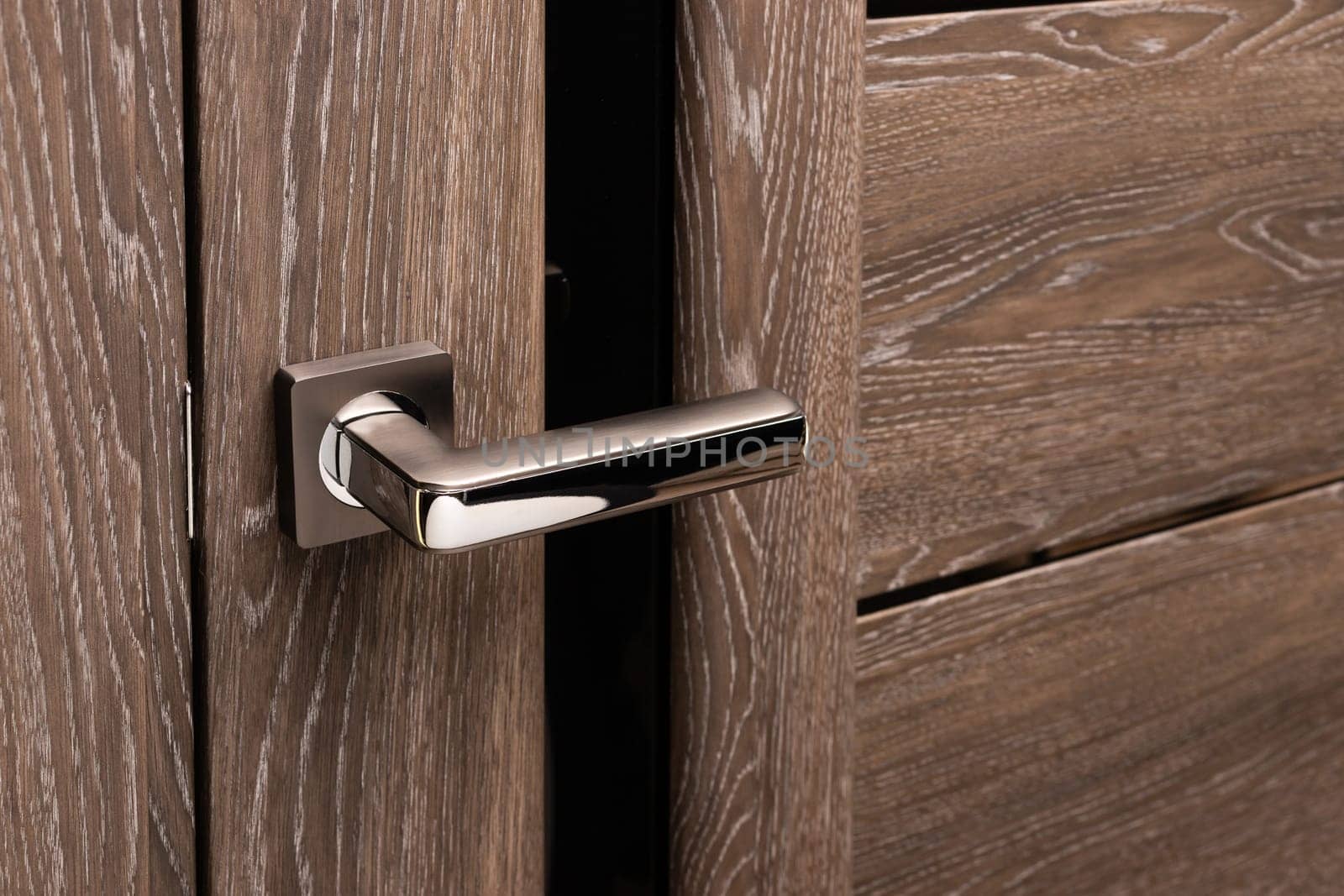 Close up of steel door handle on brown wooden door. Dark oak door with frosted glass. Concept of interior details and the choice of interior doors during the repair.
