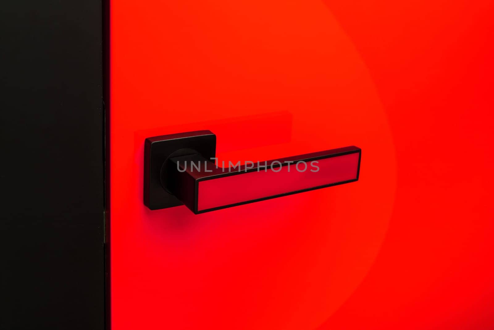 Close up of stylish matte black and red door handle on colored interior door. Handle with insert of same color as door. Bright red door for home or office. Interior details concept.