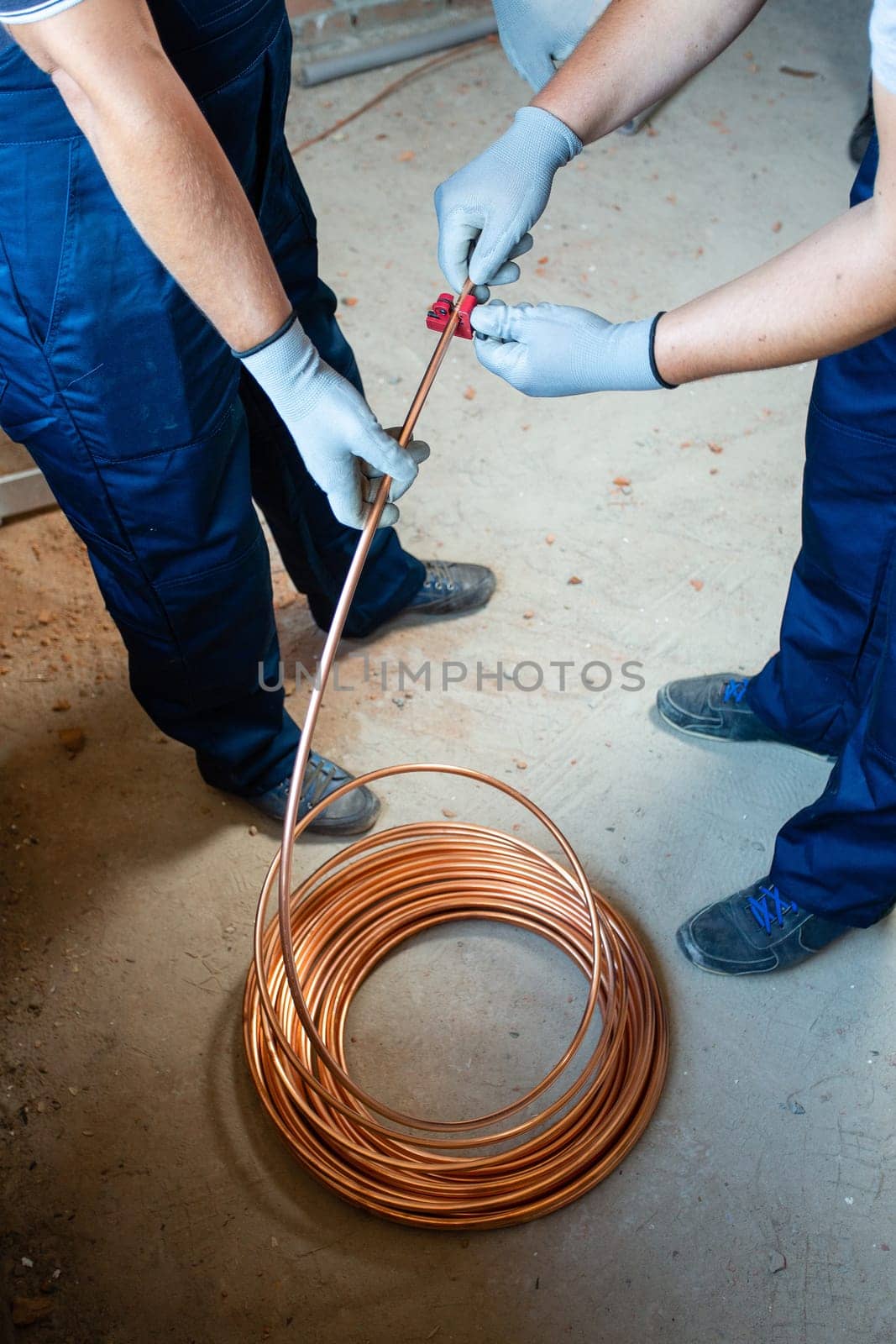 Installation works. Two men in blue overalls and protective gloves prepare underfloor heating for water heating on construction site. Construction work concept.