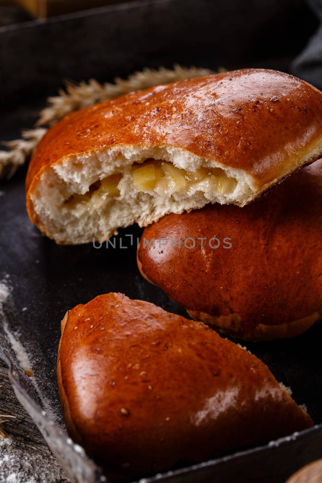 Close up of homemade buns with slices of apples inside on dark background. One broken bun in which the filling is visible lies on another bun. Concept of homemade sweet pastries and fruit fillings.